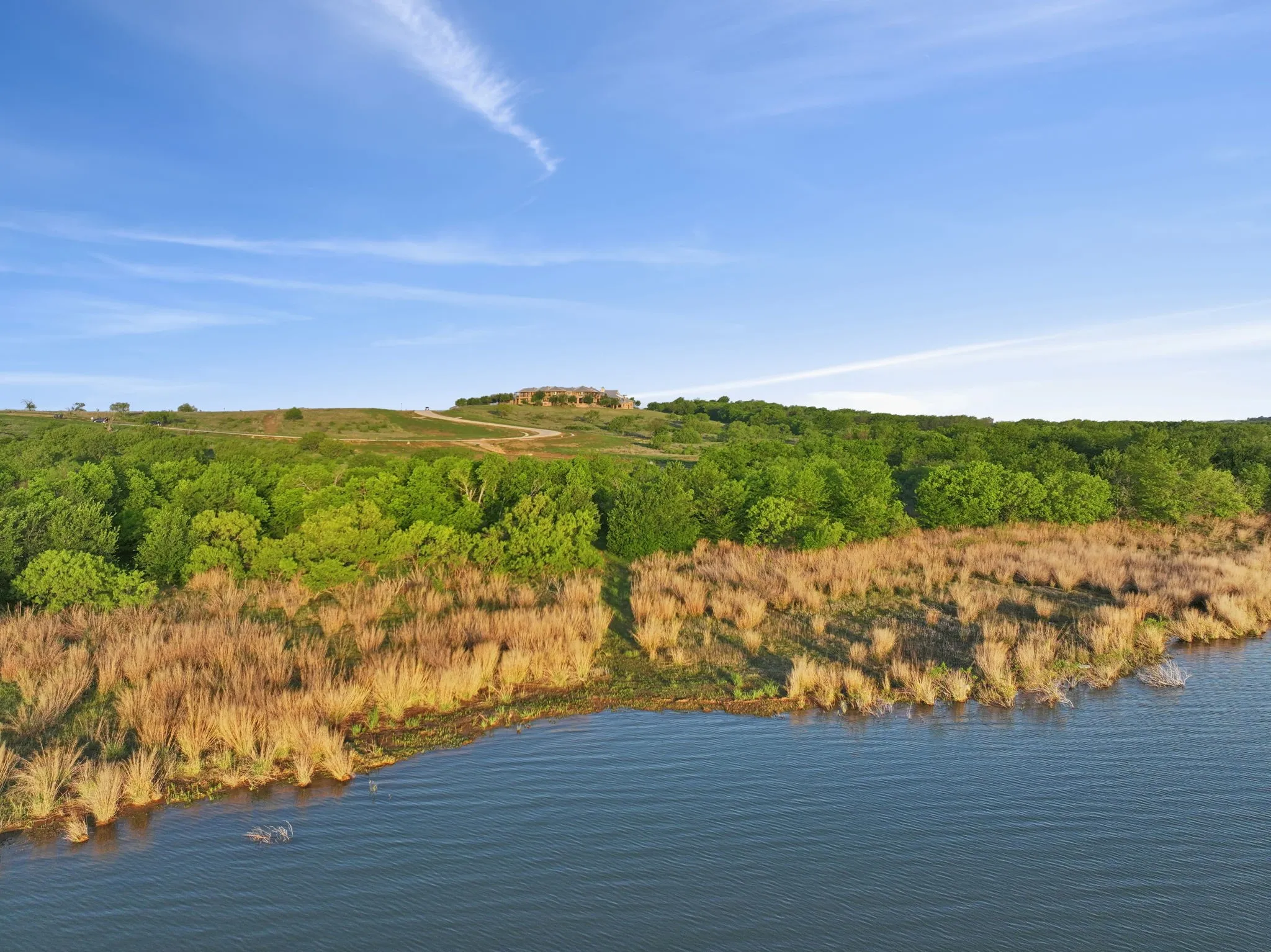 Waterfront property featuring a gently sloping hillside, mature trees, and a distant structure on an elevated terrain