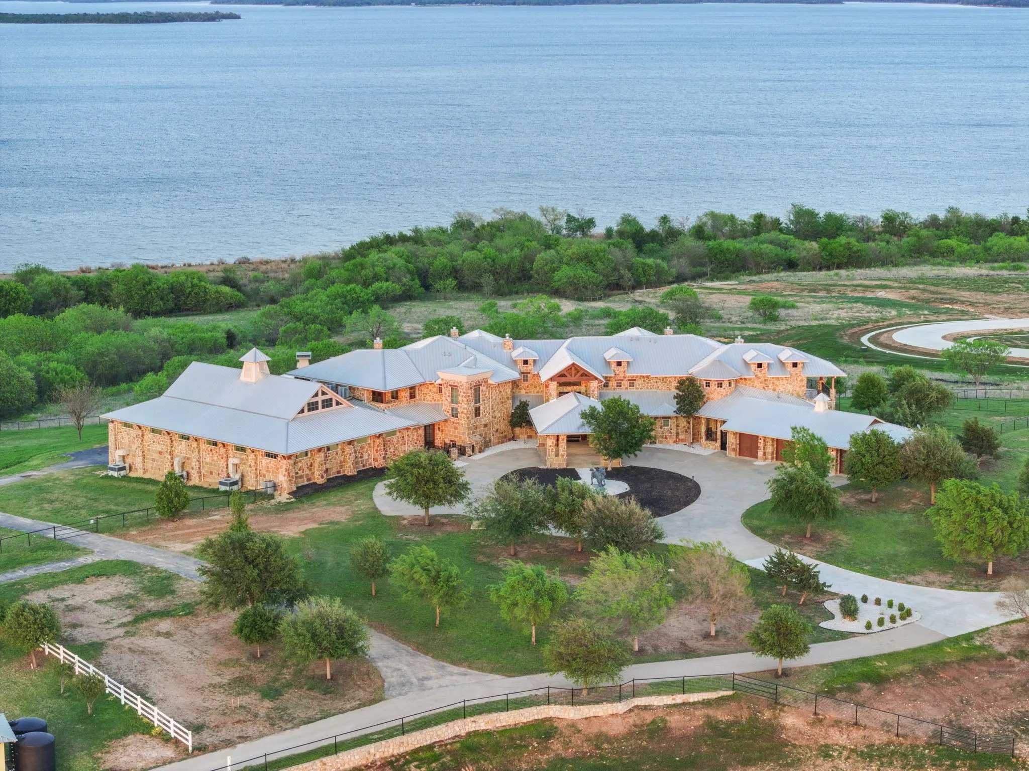 Stone exterior residence with multiple gables and dormer windows, featuring a circular driveway and mature landscaping