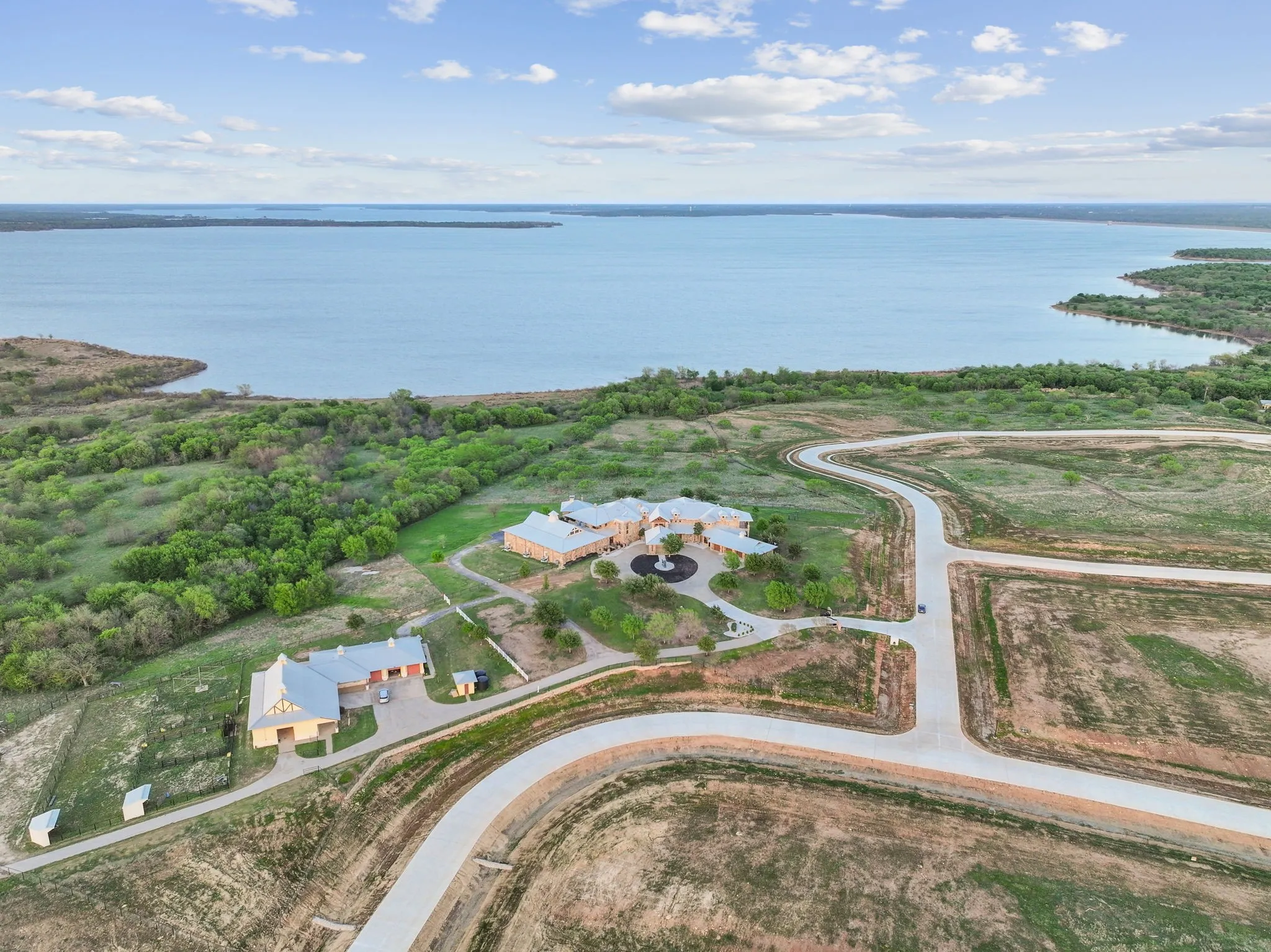 Expansive waterfront property featuring a large residence, separate outbuilding, and winding paved roads