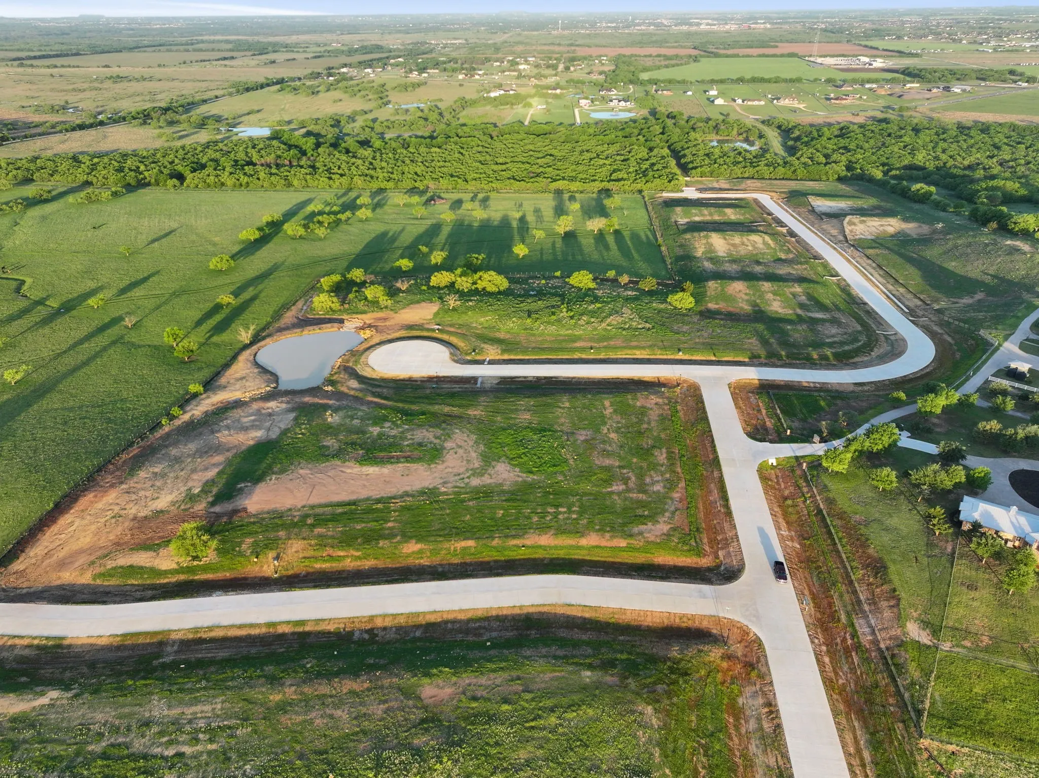 Aerial perspective of expansive land parcels featuring paved roads and a retention pond