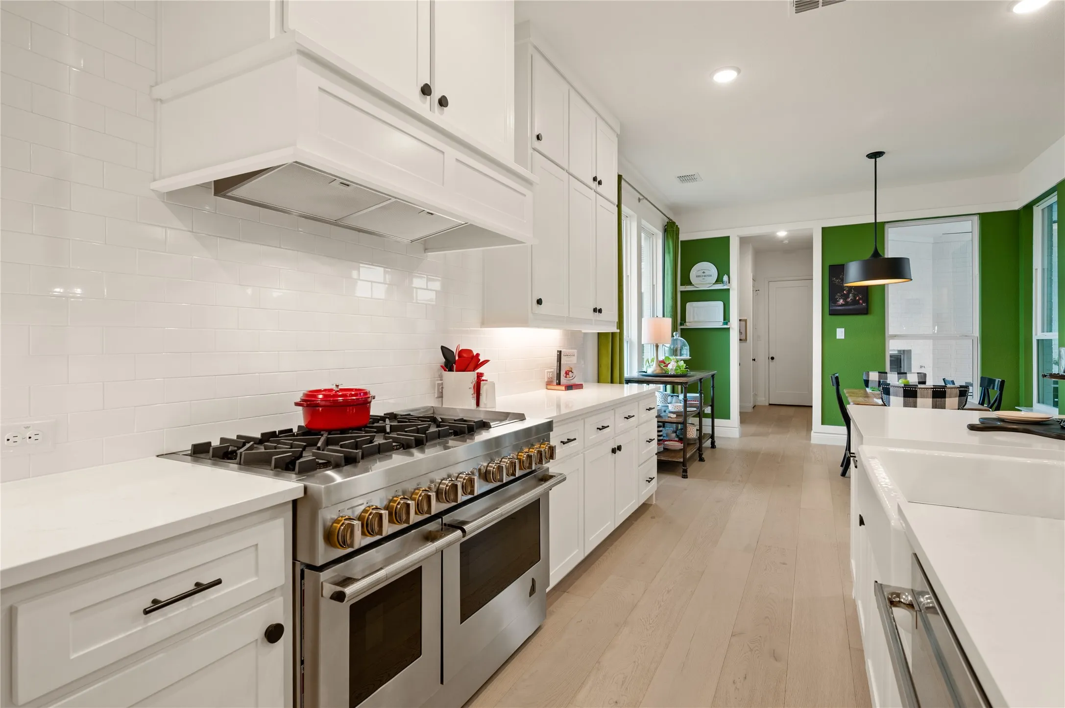 Gourmet kitchen featuring an expansive island with seating, white shaker cabinetry, light wood flooring, a stainless steel refrigerator, custom white subway tile backsplash, custom gas appliances, and more