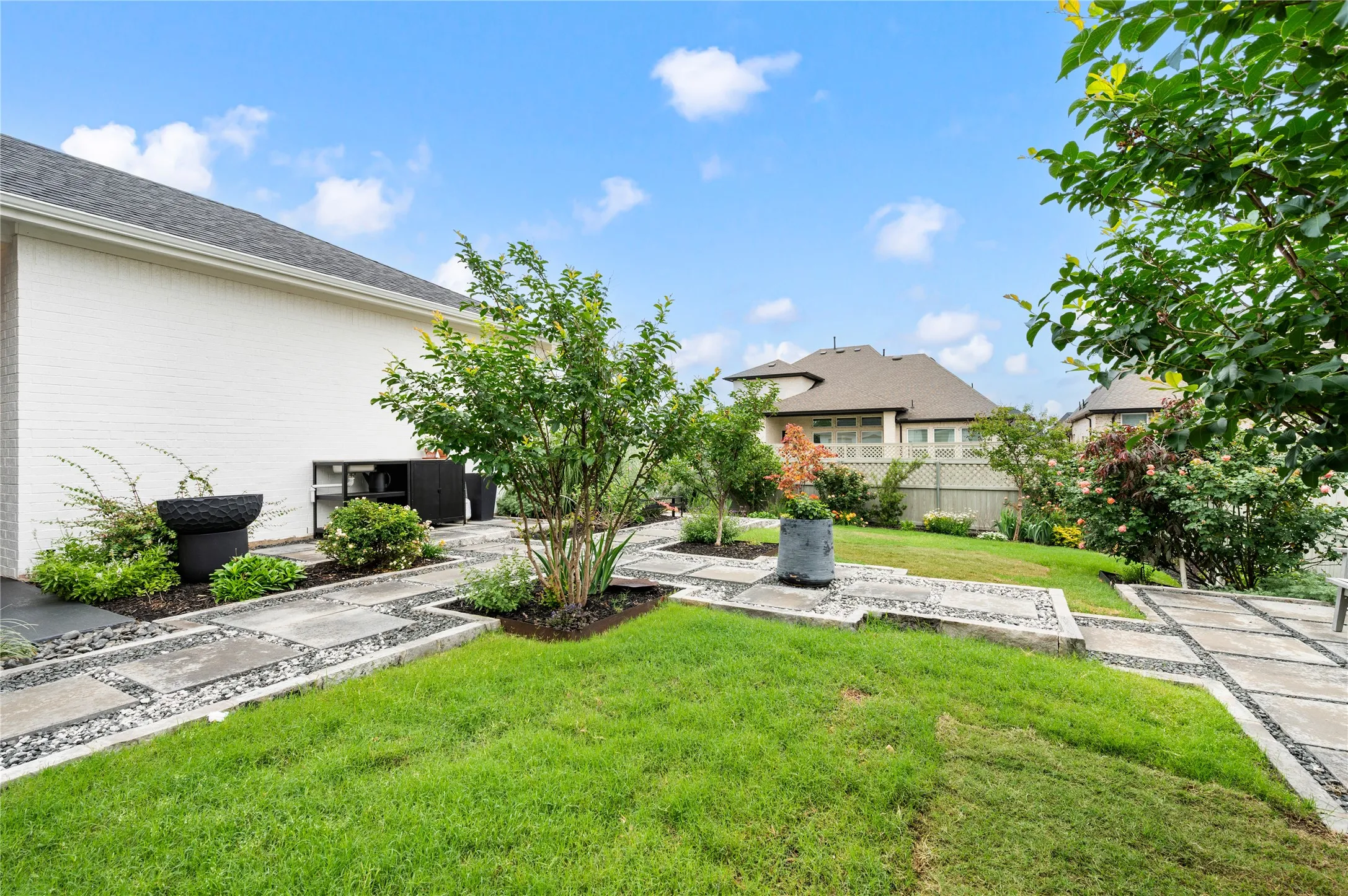 Manicured lawn, paver and gravel pathways, perimeter plantings, mature trees, and a white brick exterior