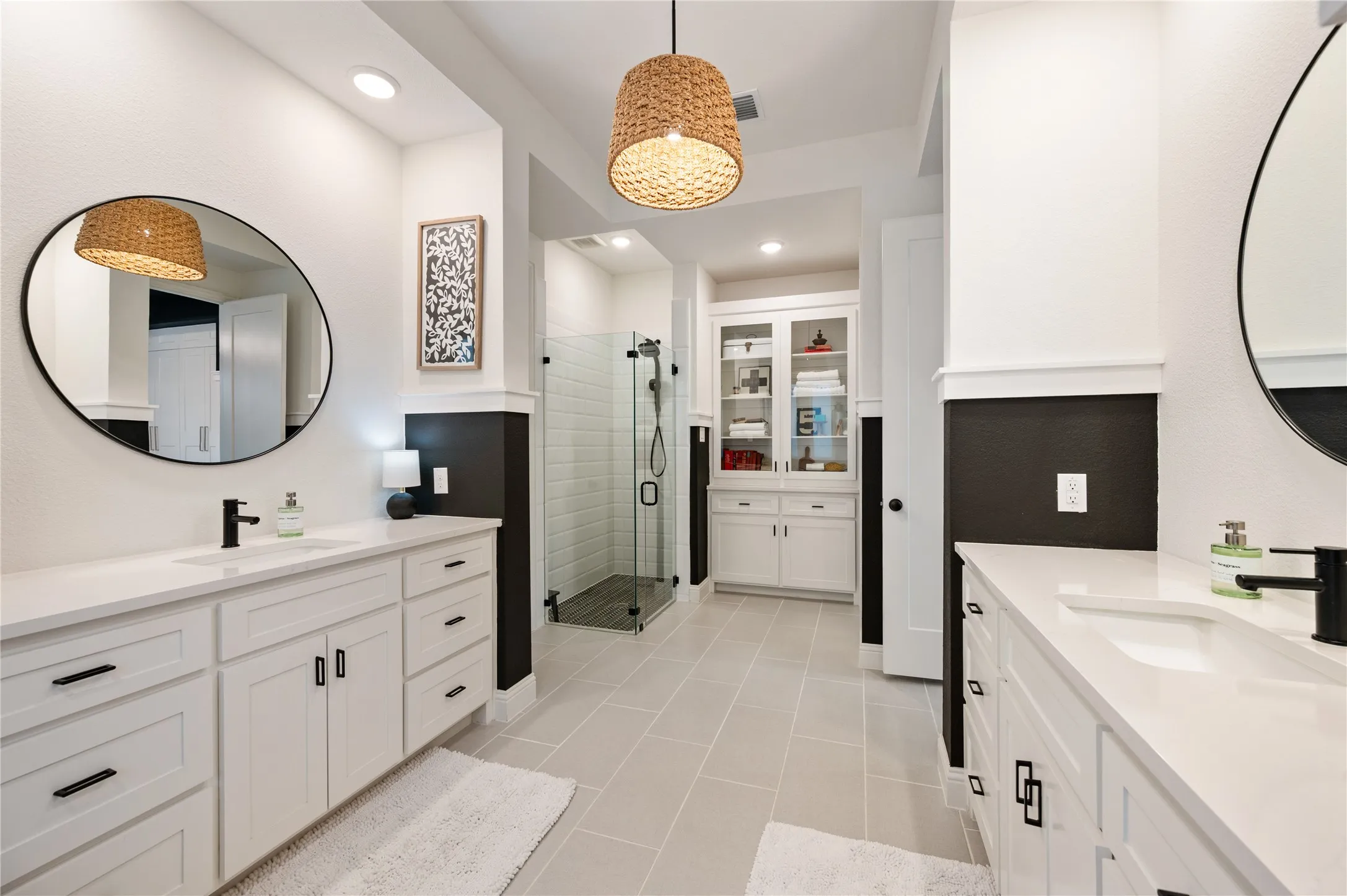 Contemporary bathroom featuring dual vanities with white cabinetry, quartz countertops, and matte black fixtures with tile flooring, plenty of natural light and a seperate shower and built in custom linen and medicine cabinet.