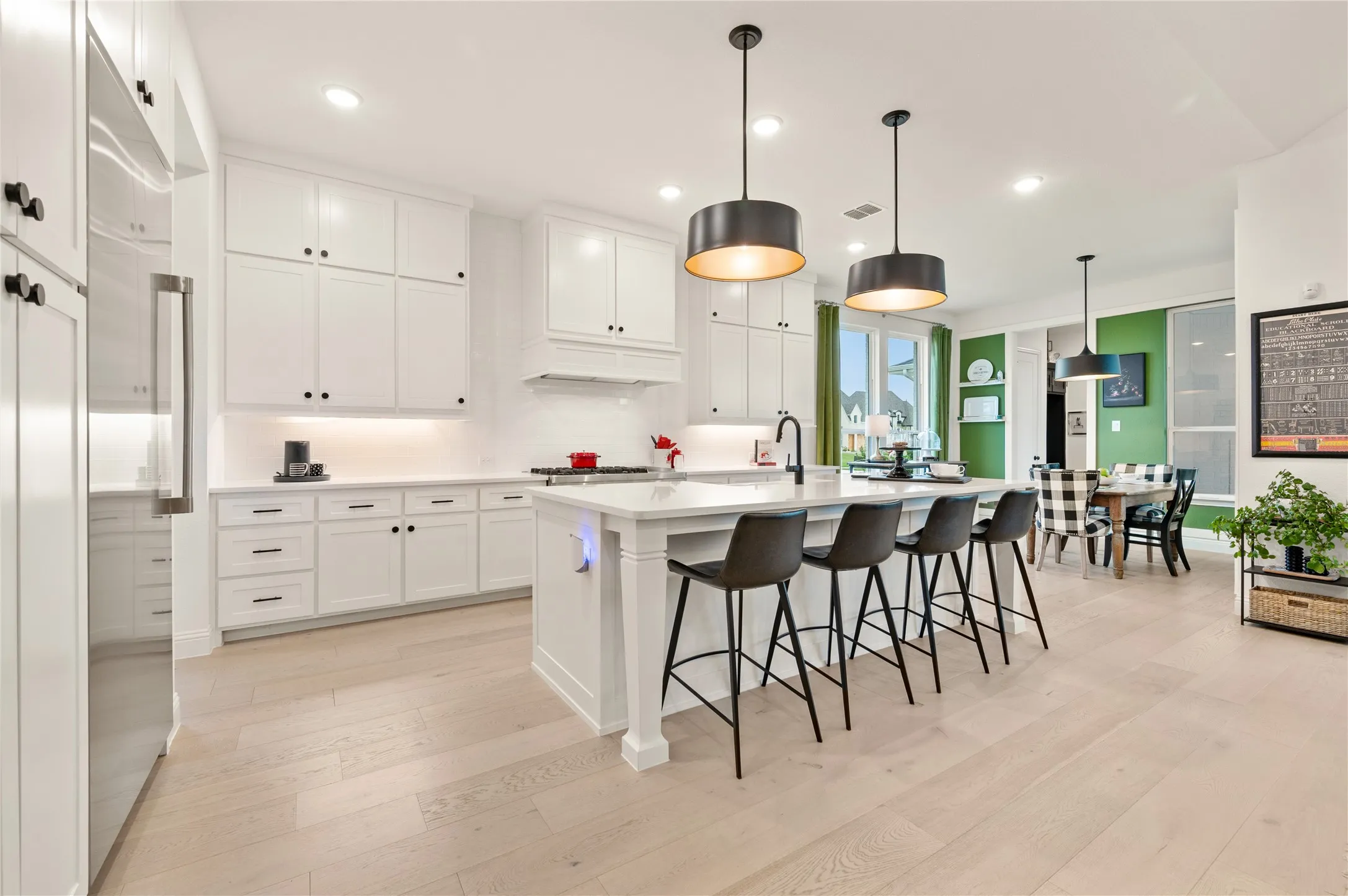 Gourmet kitchen featuring an expansive island with seating, white shaker cabinetry, light wood-finish flooring, a stainless steel refrigerator, custom white subway tile backsplash, custom gas appliances, and more