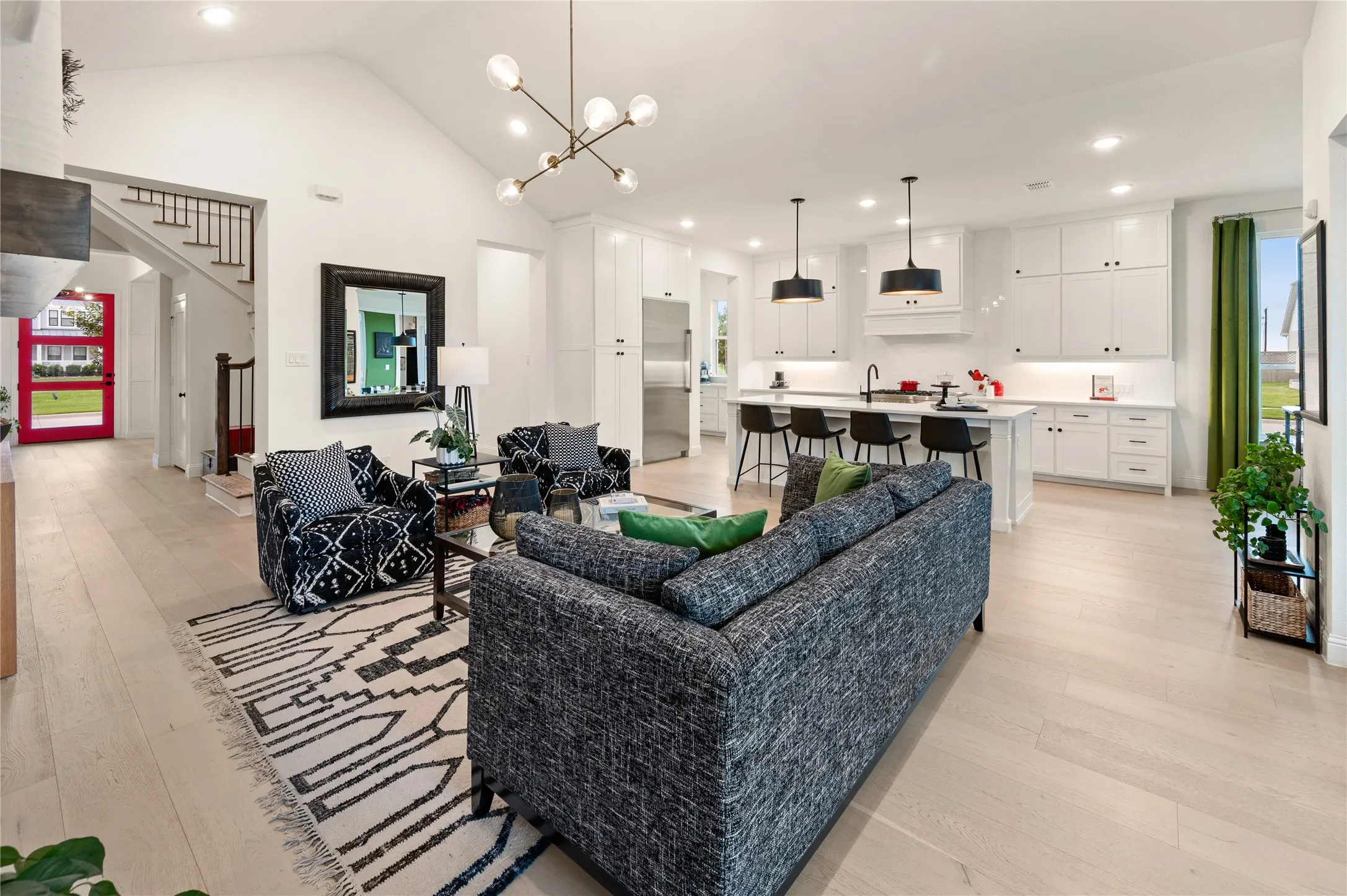 Expansive open-concept living area featuring vaulted ceilings, light wood-finish flooring, and a contemporary linear chandelier