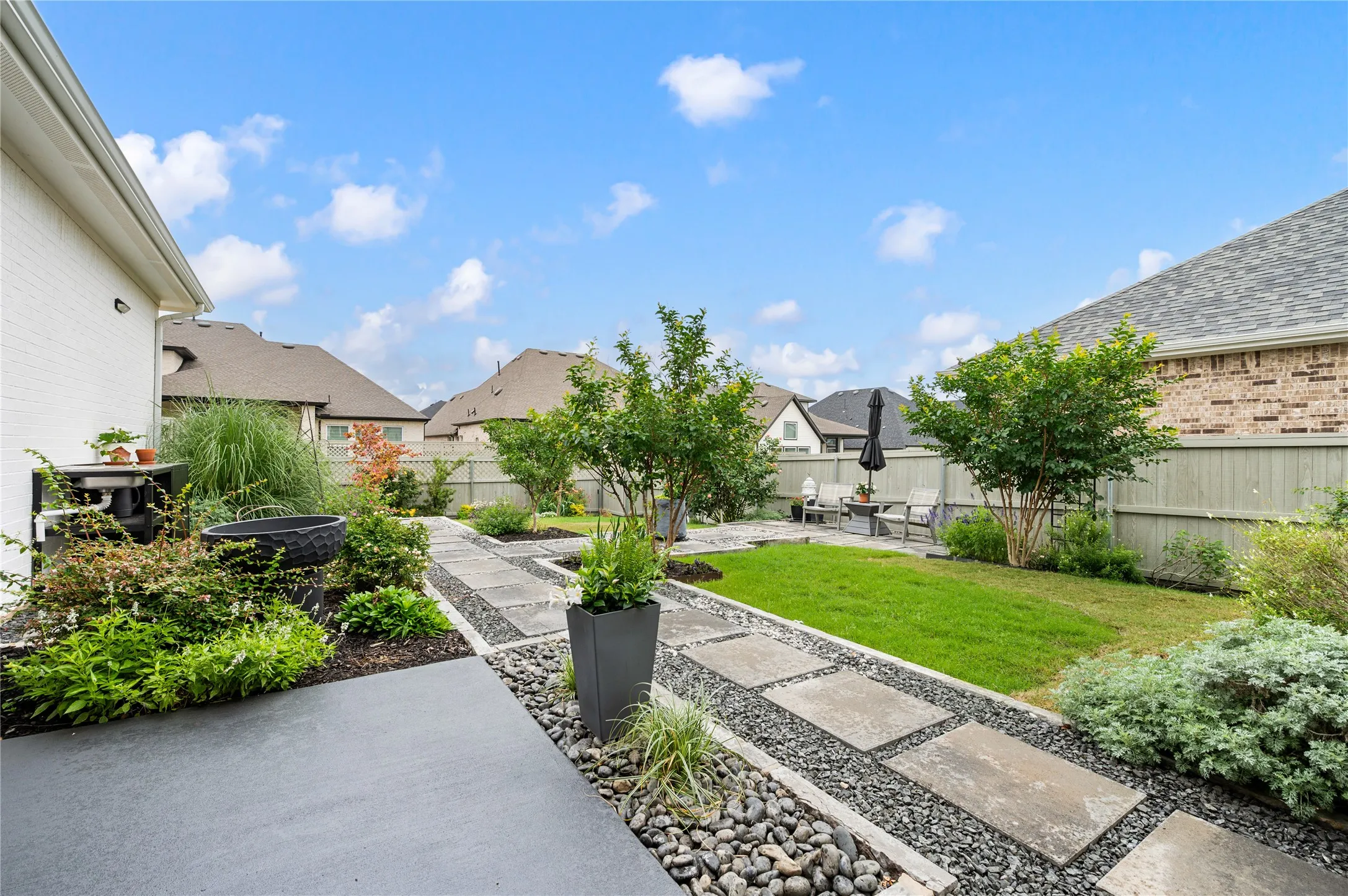 Expansive backyard featuring a stained and sealed oncrete patio, landscaped garden beds, stepping stone pathways and a well-maintained lawn with covered outdoor seating and a fireplace.