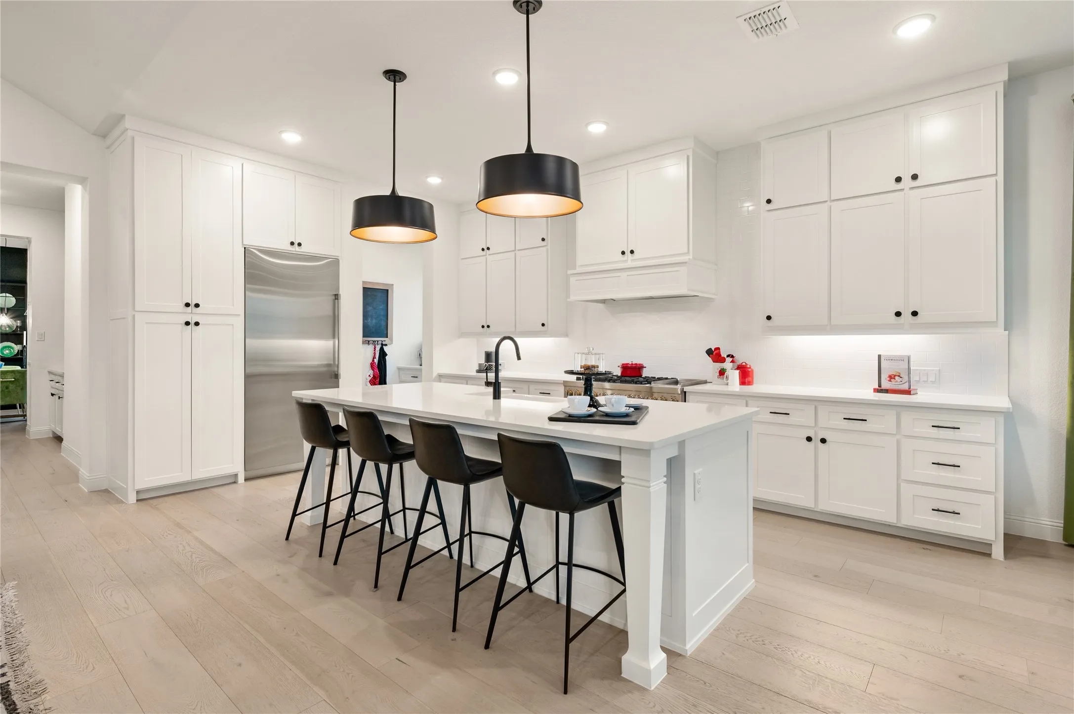 Gourmet kitchen featuring an expansive island with seating, white shaker cabinetry, light wood-finish flooring, a stainless steel refrigerator, custom white subway tile backsplash, custom gas appliances, and more
