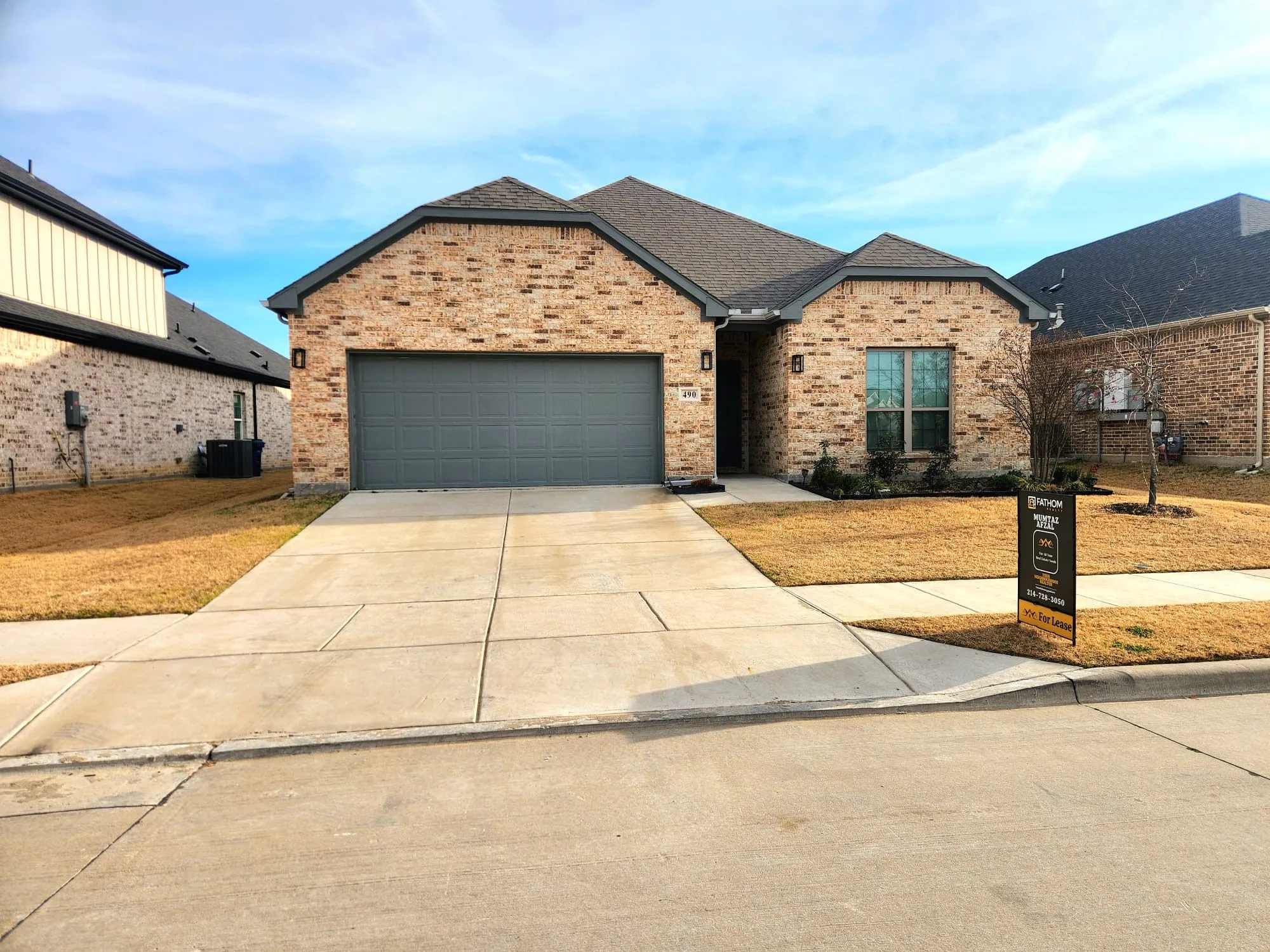 Brick facade residence featuring an attached garage with a dark gray door, a concrete driveway, and a gabled roofline