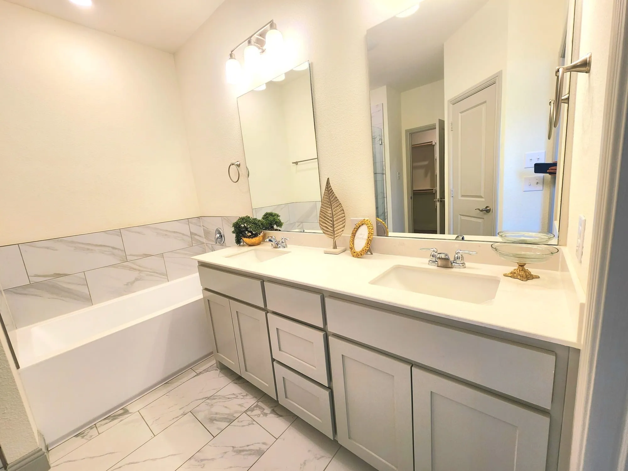 Bathroom featuring a dual vanity with light-toned cabinetry and integrated sinks, a tub with a tiled surround, a large wall-mounted mirror, and tile flooring