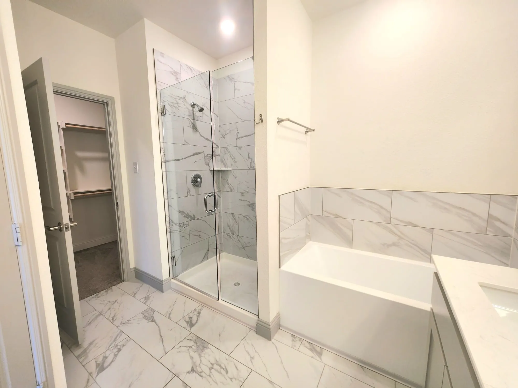 Full bathroom featuring a glass-enclosed shower with tile surround, a soaking tub with tile wainscoting, and large format marble-look floor tiles