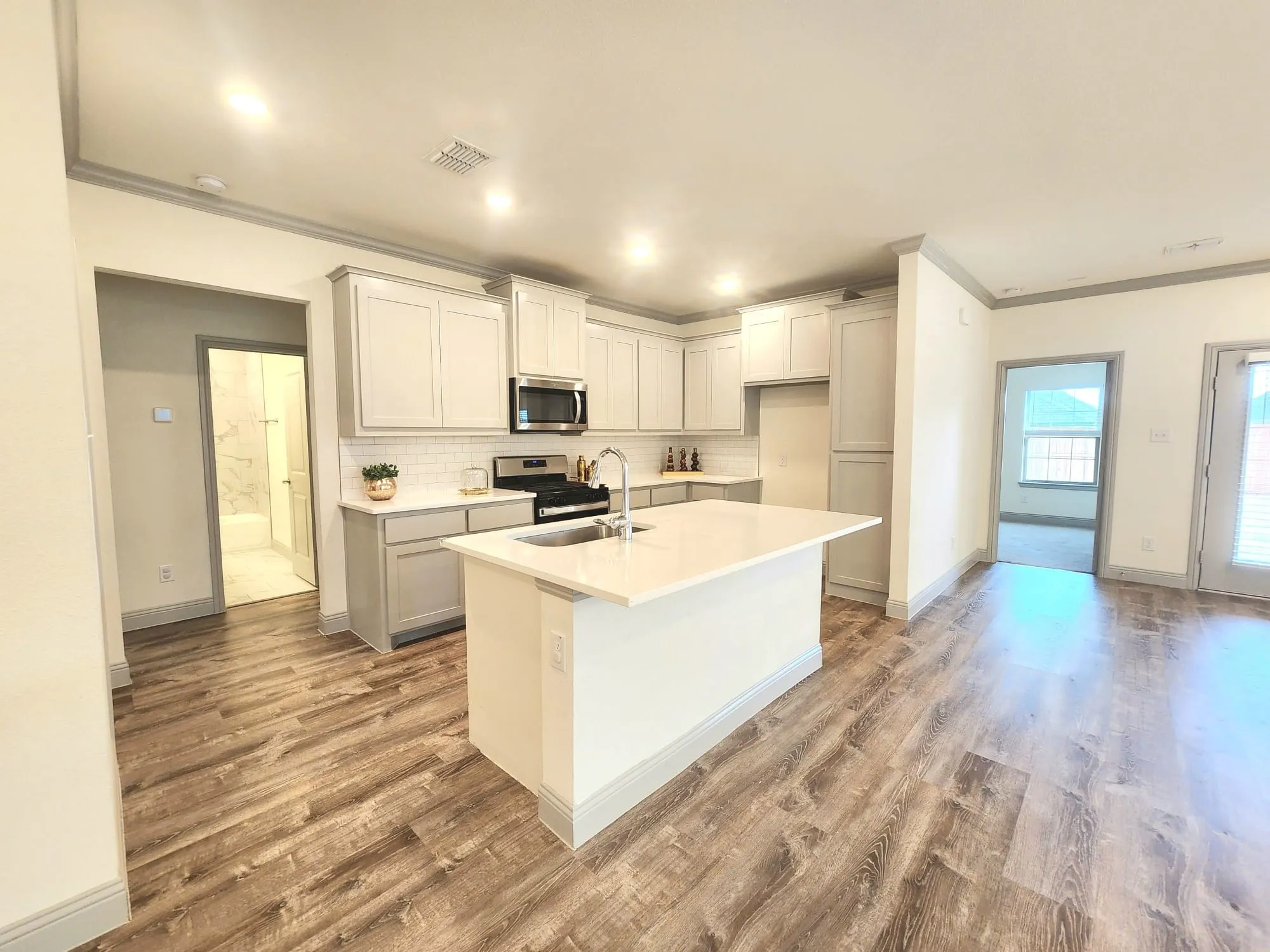 Modern kitchen featuring light cabinetry, a central island with a sink, stainless steel appliances, a white subway tile backsplash, and wood-finish flooring