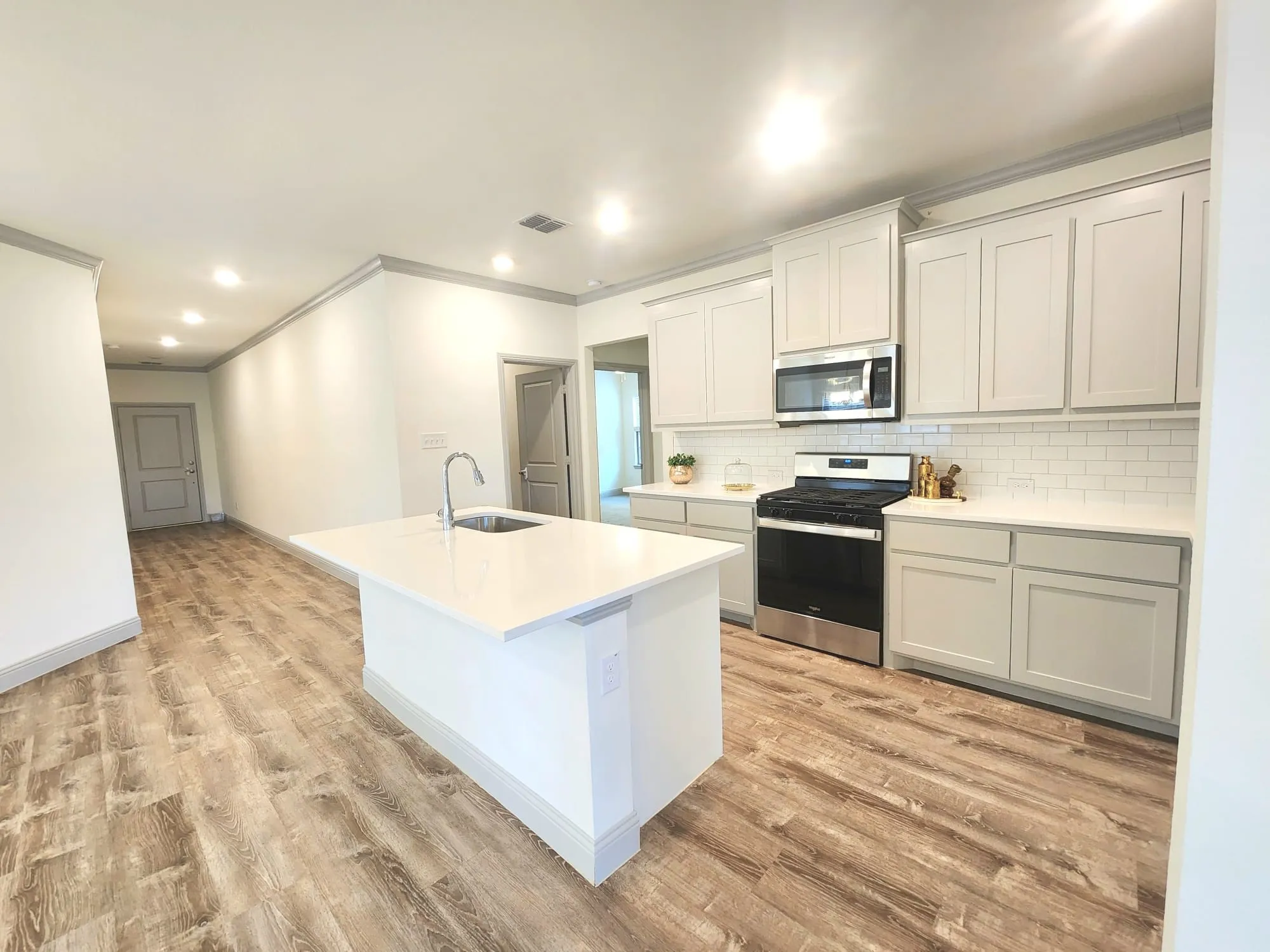 Modern kitchen featuring a central island with an undermount sink, white countertops, and white shaker-style cabinetry