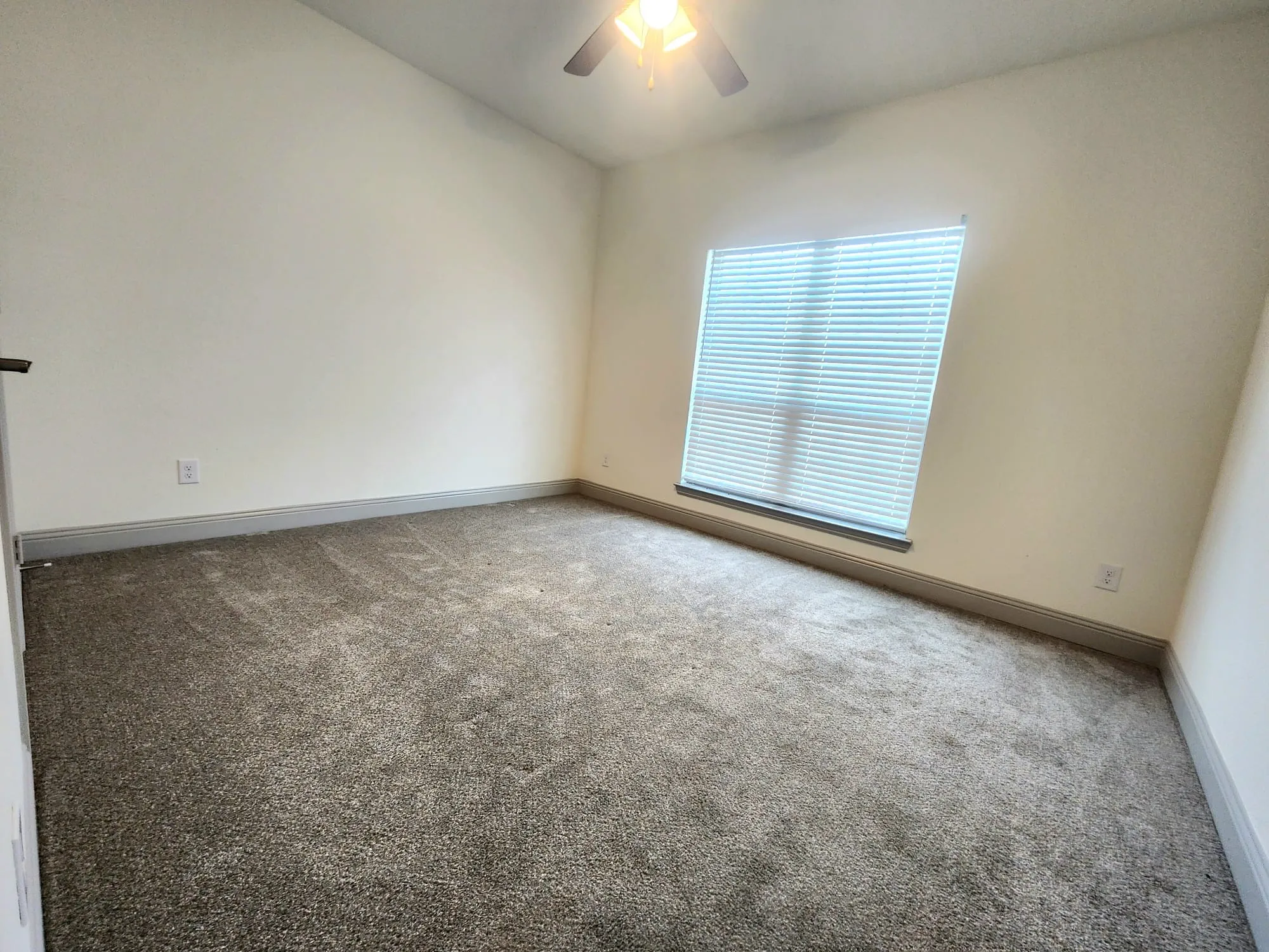 Neutral-toned carpeted room featuring a large window with horizontal blinds