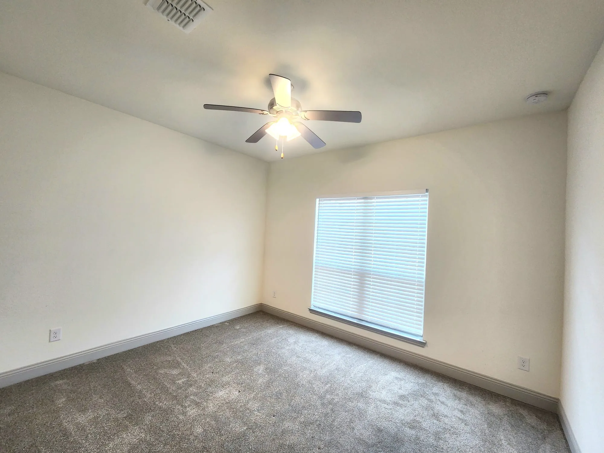 Carpeted interior room featuring a large window with horizontal blinds, a ceiling fan with integrated lighting, and neutral wall tones