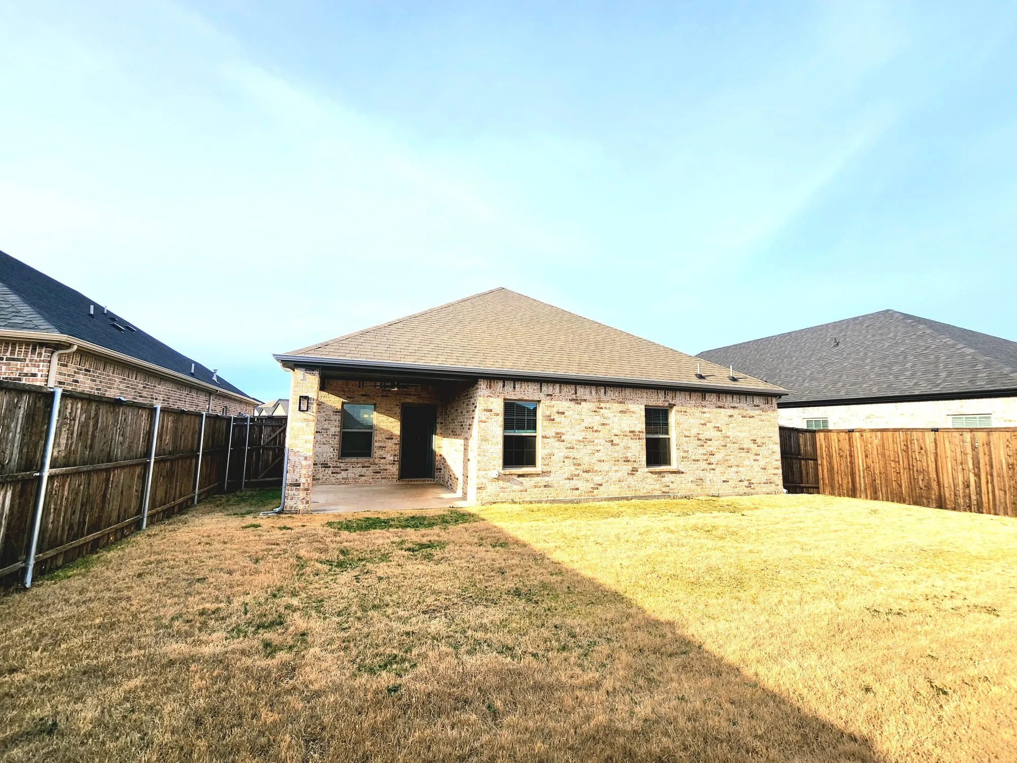 Backyard featuring a covered patio with concrete flooring, brick exterior, and a wood privacy fence