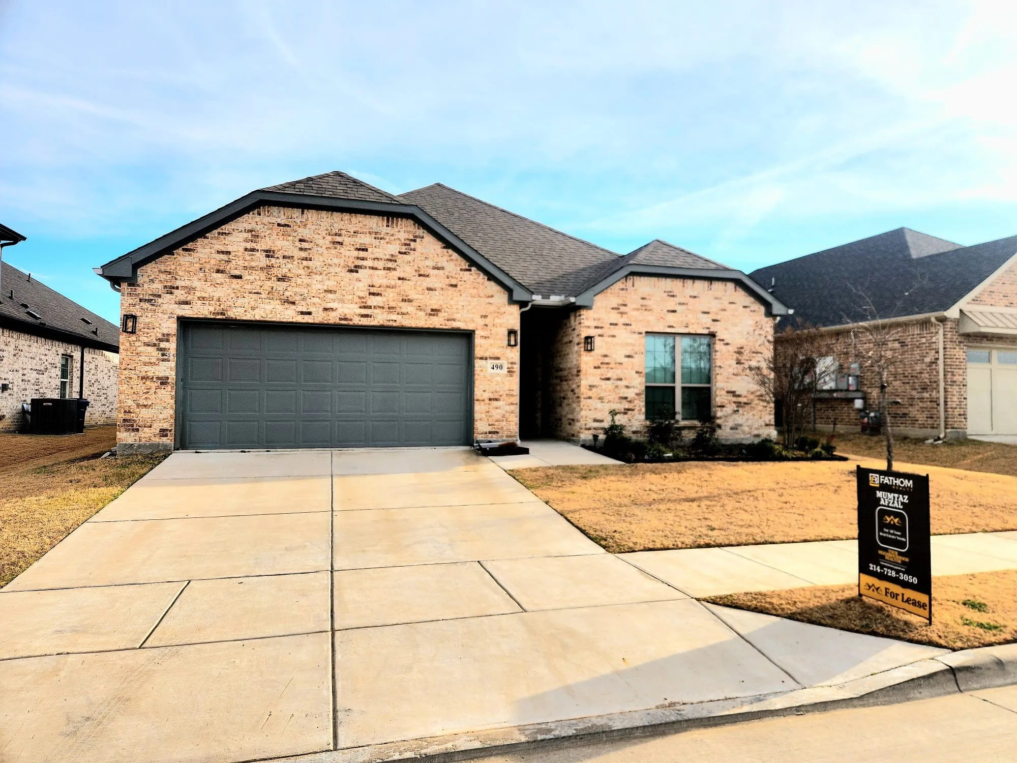 Brick facade residence featuring a dark gray garage door, concrete driveway, and a small landscaped area with low-lying shrubs