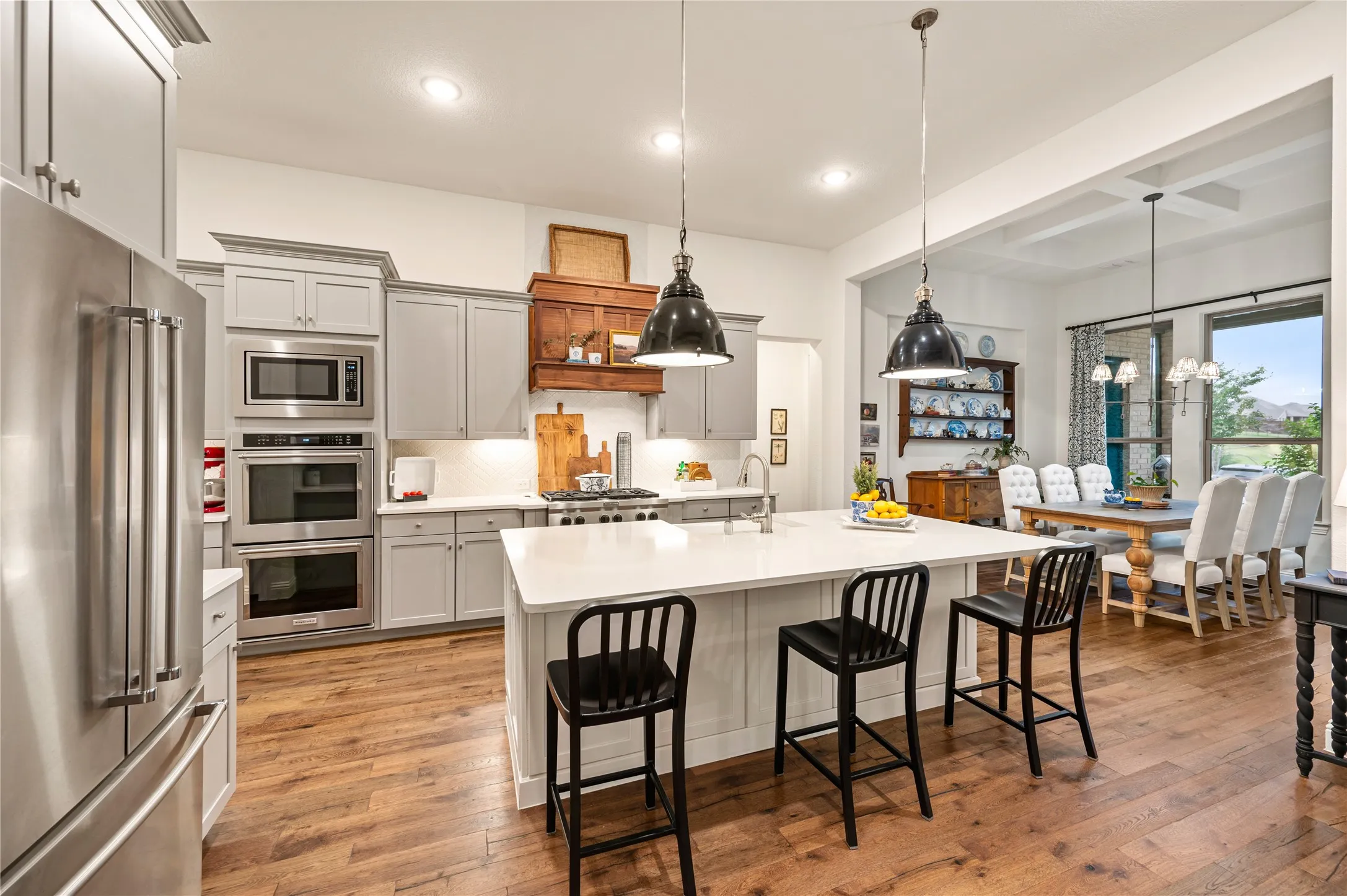 Gorgeous high end kitchen with large island, custom wood vent hood, modern painted cabinets, ss gas appliances, double oven, custom pendants and natural light throughout