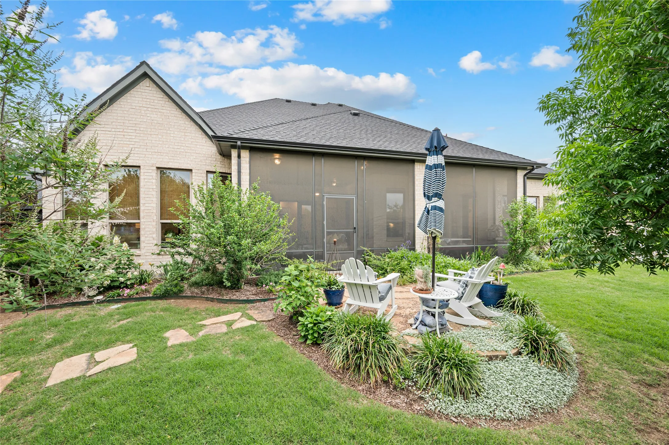 Rear exterior featuring a screened patio with a brick paver seating area, surrounded by diverse plantings, the natural side of wildridge and no neighbors!