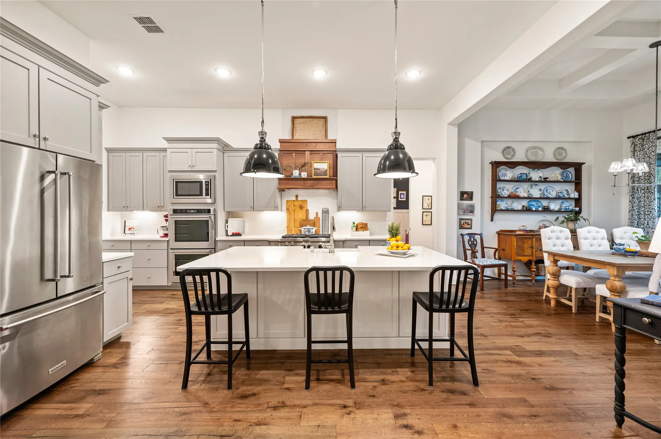 Gorgeous high end kitchen with large island, custom wood vent hood, modern painted cabinets, ss gas appliances, double oven, custom pendants and natural light throughout