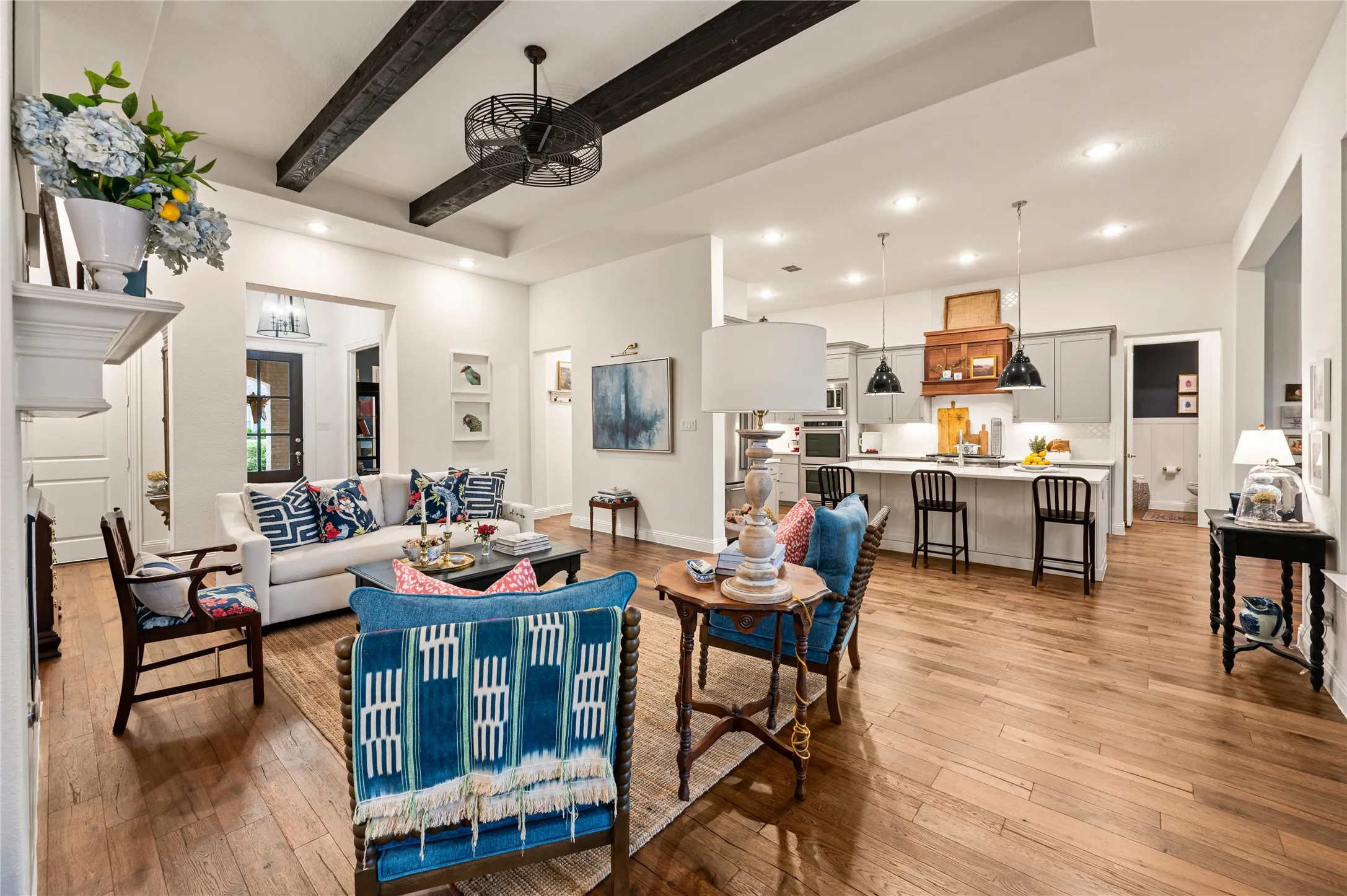 Open-concept living space featuring wood flooring, exposed ceiling beams, recessed lighting, and a modern ceiling fan with views of kitchen and dining space
