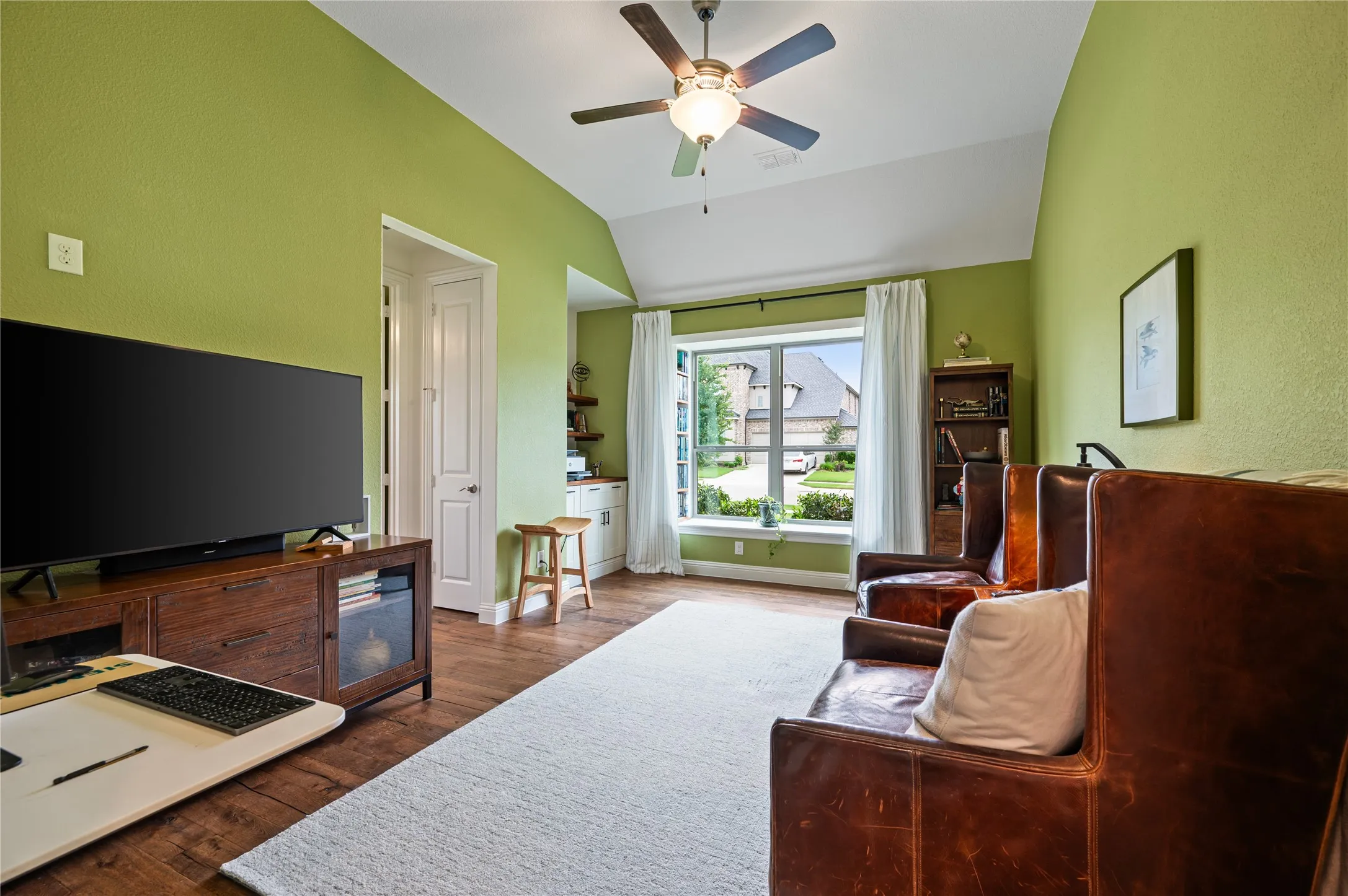 Generational suite living room featuring wood-flooring, elevated ceiling, custom shelving and storage, custom bookshelves and bench seating in window.