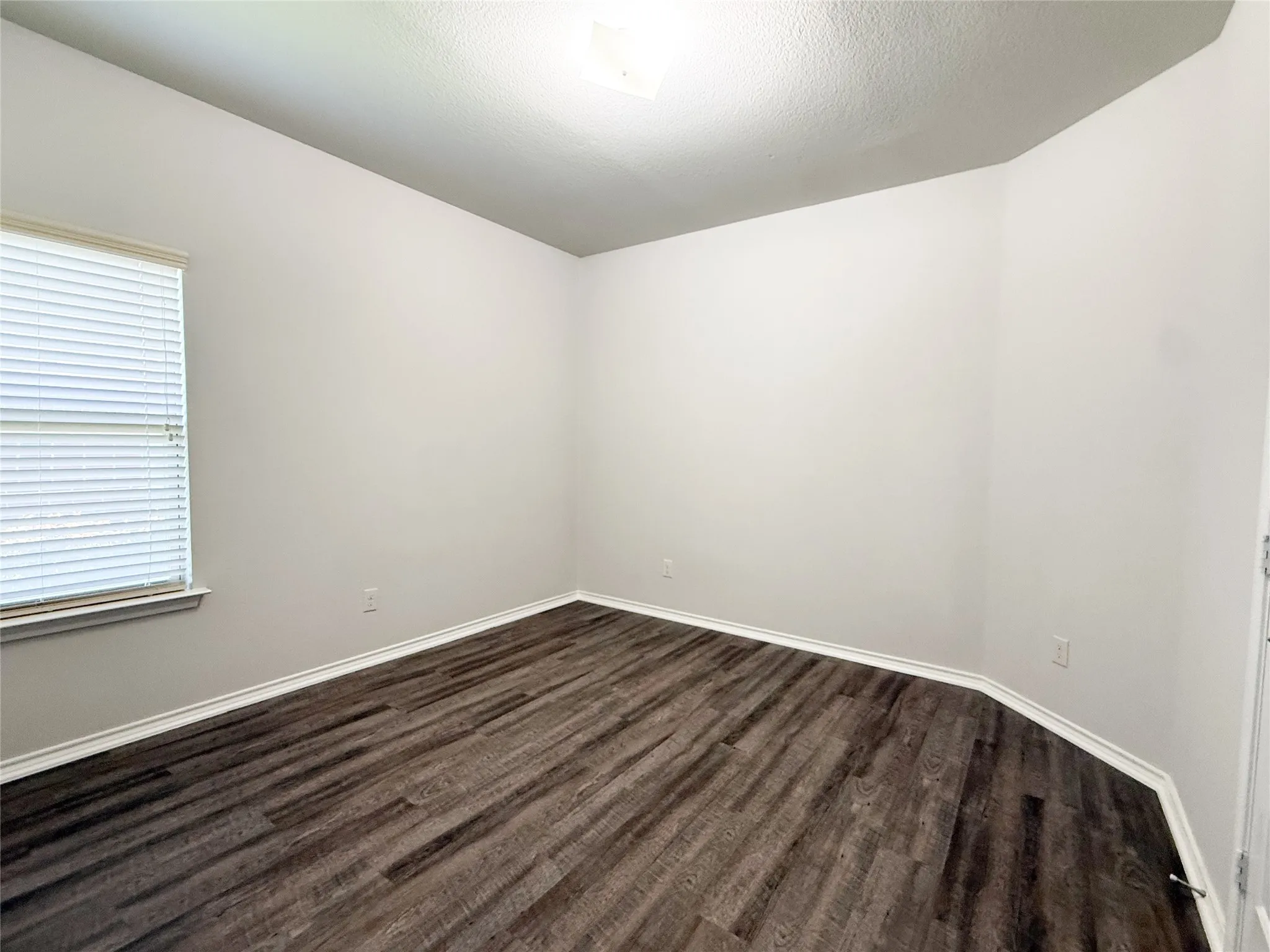 Room featuring dark wood-finish flooring, light neutral-toned walls, a window with blinds, and white baseboards