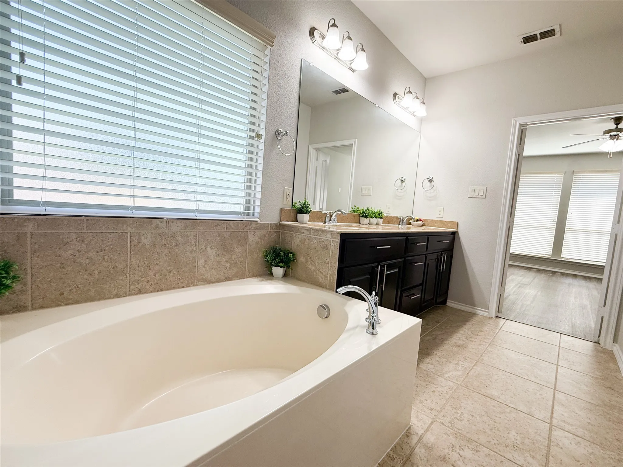 Soaking tub with chrome fixtures, tiled surround, and a window with blinds
