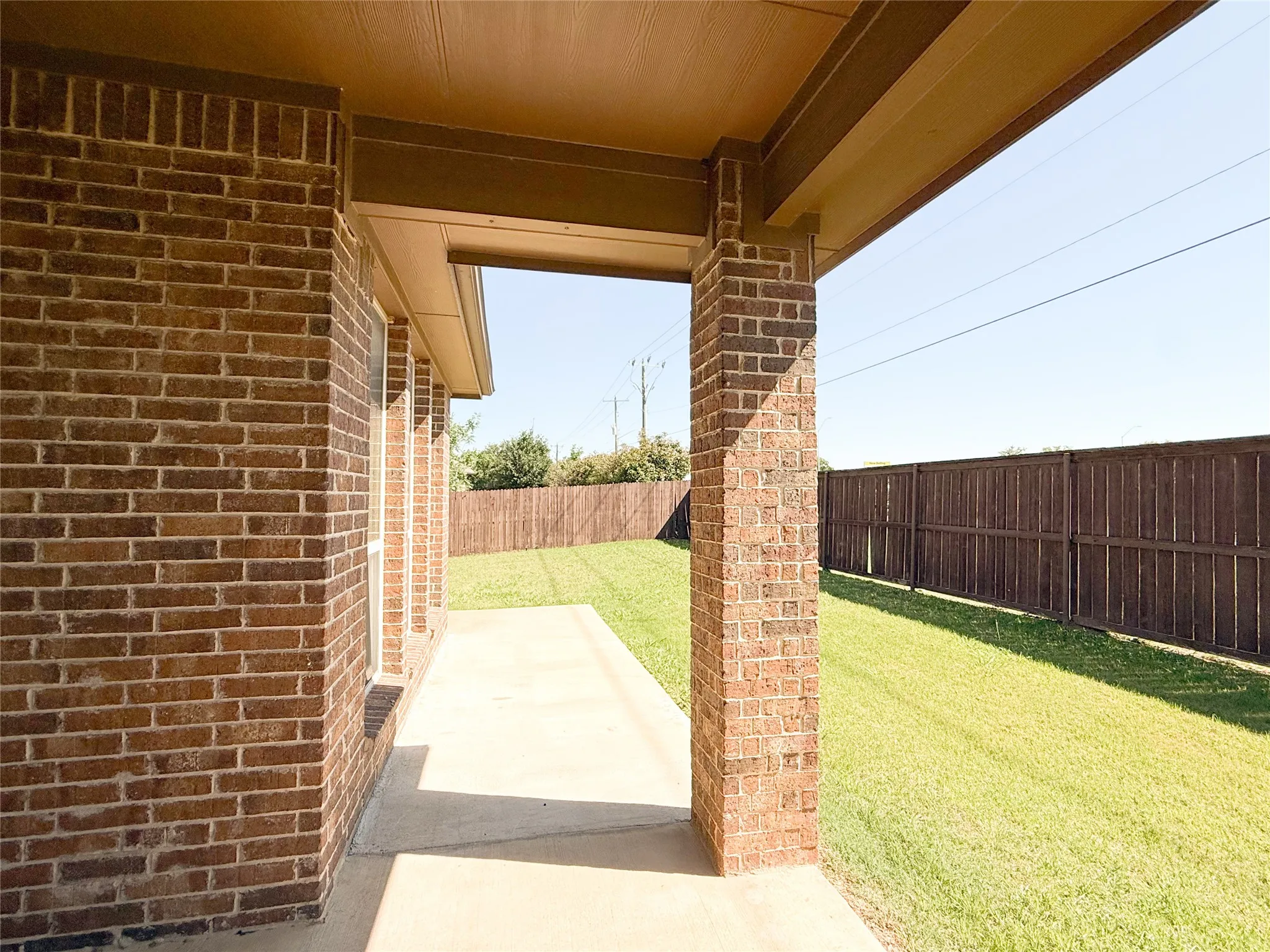 Covered patio featuring brick columns, a concrete surface, and direct access to a grassy yard