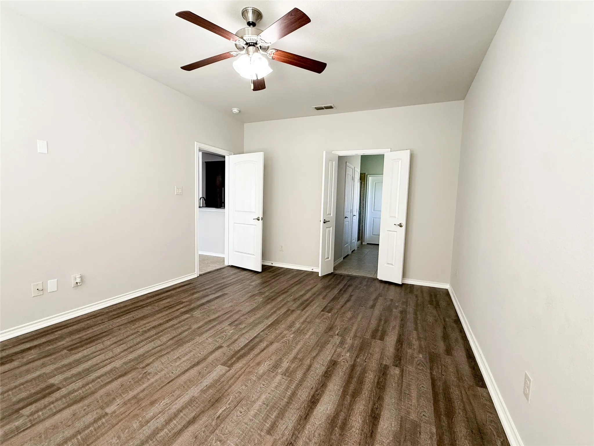 Spacious room featuring wood-finish flooring, light neutral wall tones, white trim, and a ceiling fan with integrated lighting