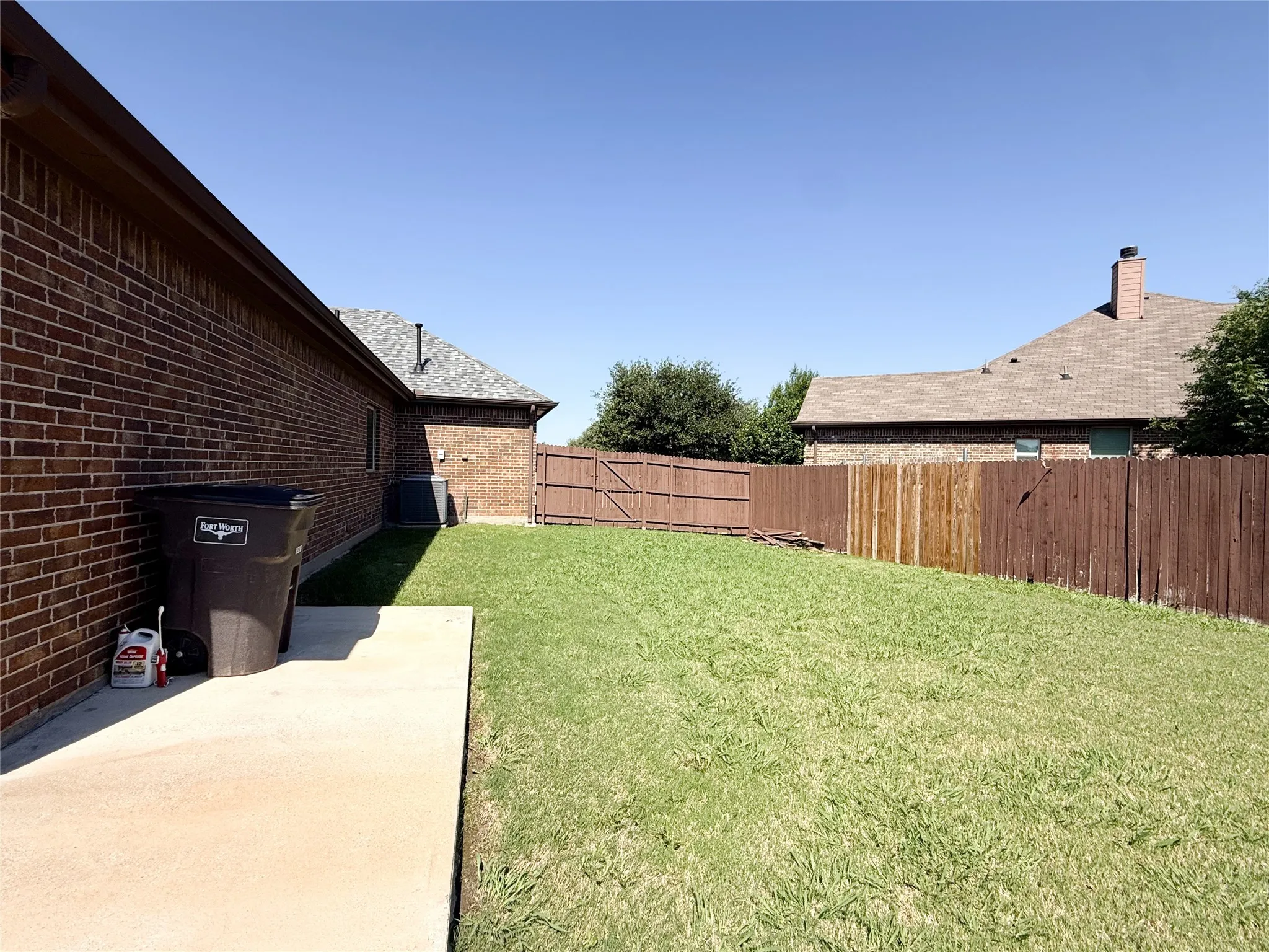 Expansive green lawn area featuring a concrete pad, brick exterior, and wood privacy fencing