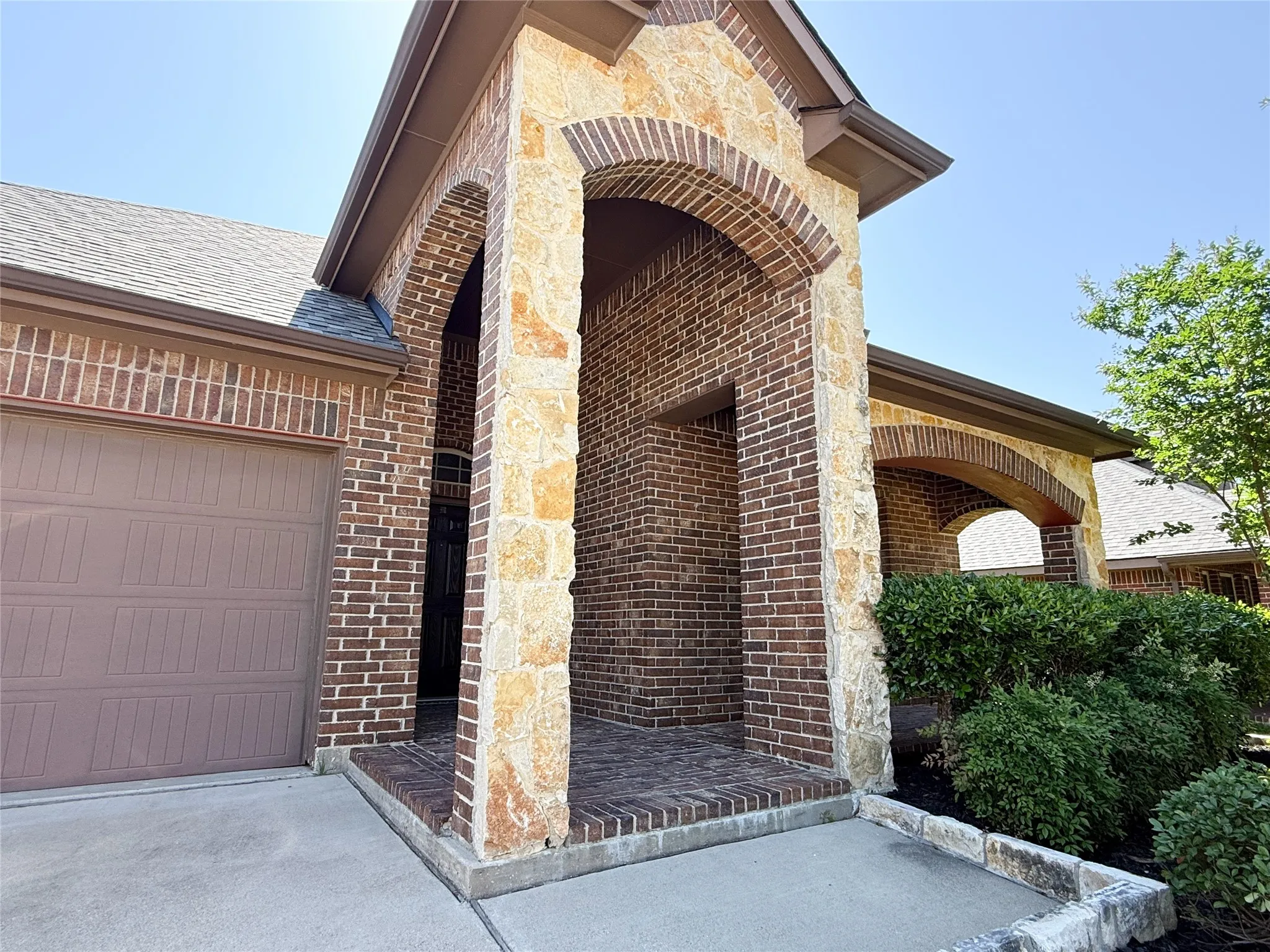 Inviting architectural details featuring a brick and stone facade, arched entryway, and dark wood-finish front door