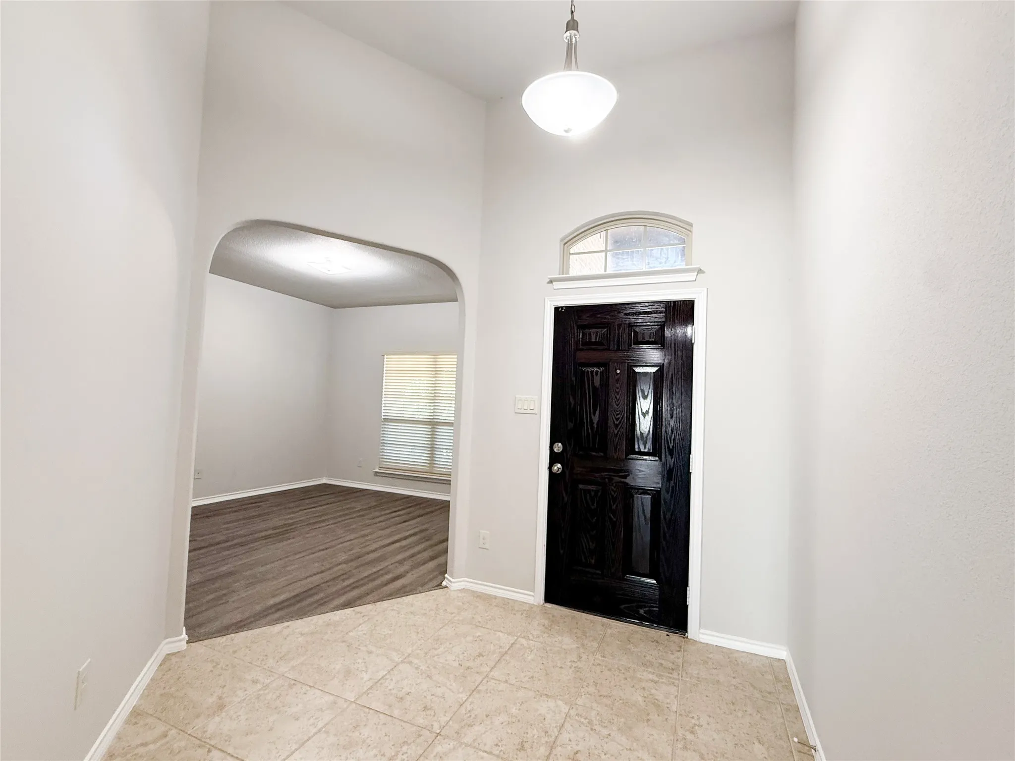 Foyer featuring an arched entryway, natural stone tile flooring, and a dark paneled entry door with an arched transom window