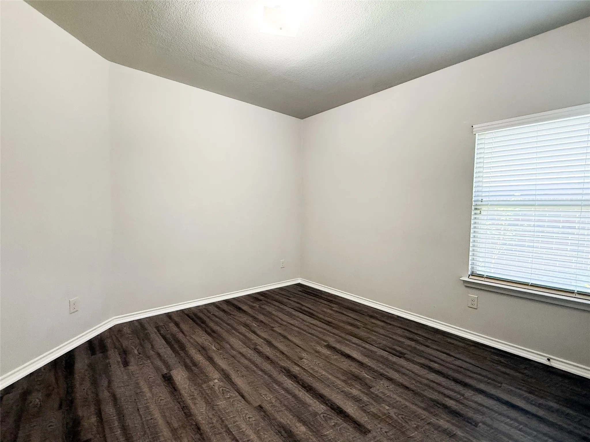 Room featuring wood-finish flooring, light-toned walls, and a window with blinds