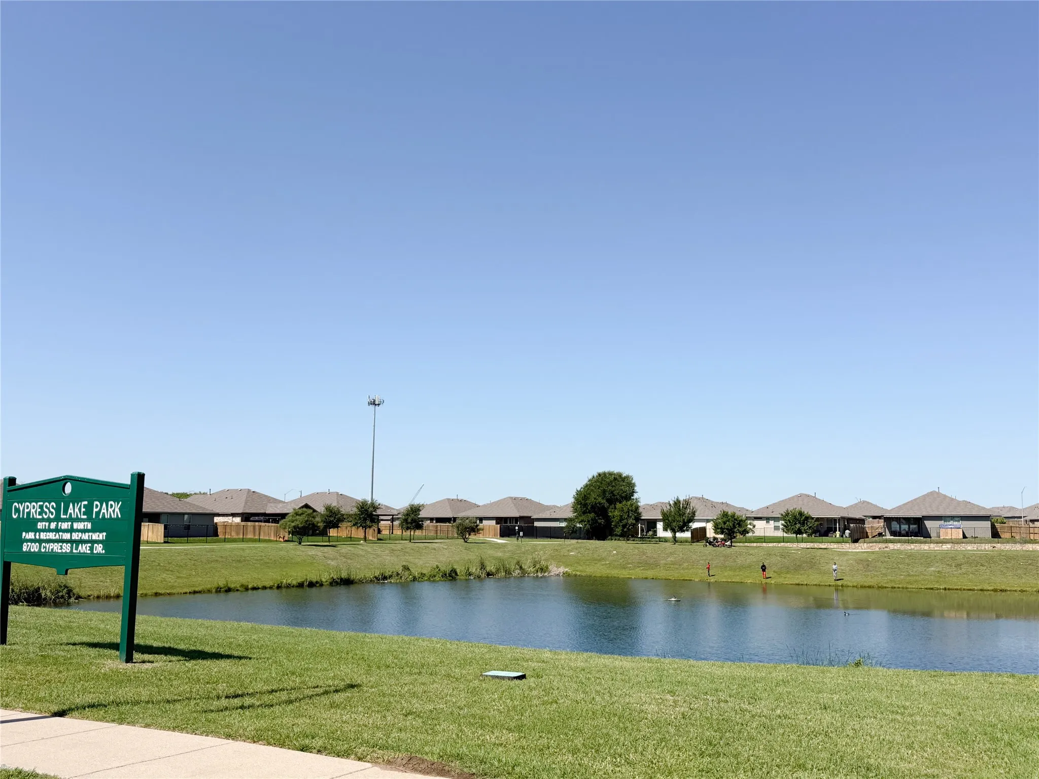 Cypress Lake Park entrance featuring a tranquil lake, expansive grassy areas, and a paved pathway