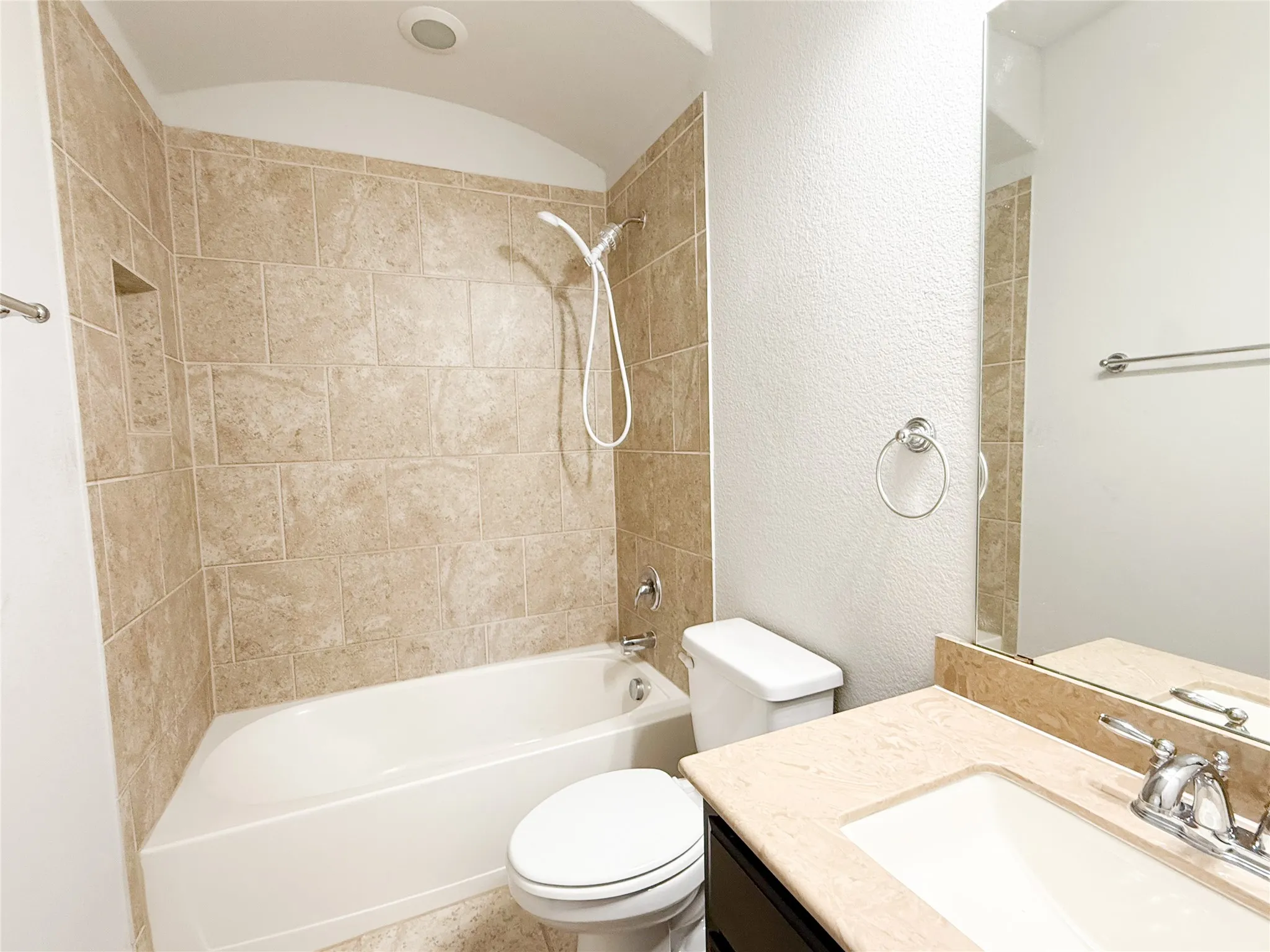 Bathroom featuring a built-in tub with tile surround, an integrated wall niche, a vanity with a light-toned countertop, and a large wall-mounted mirror