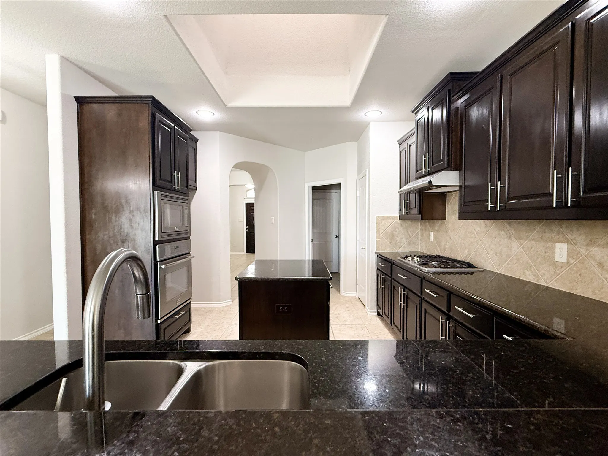 Kitchen featuring dark wood-finish cabinetry, black stone countertops, and a full tile backsplash
