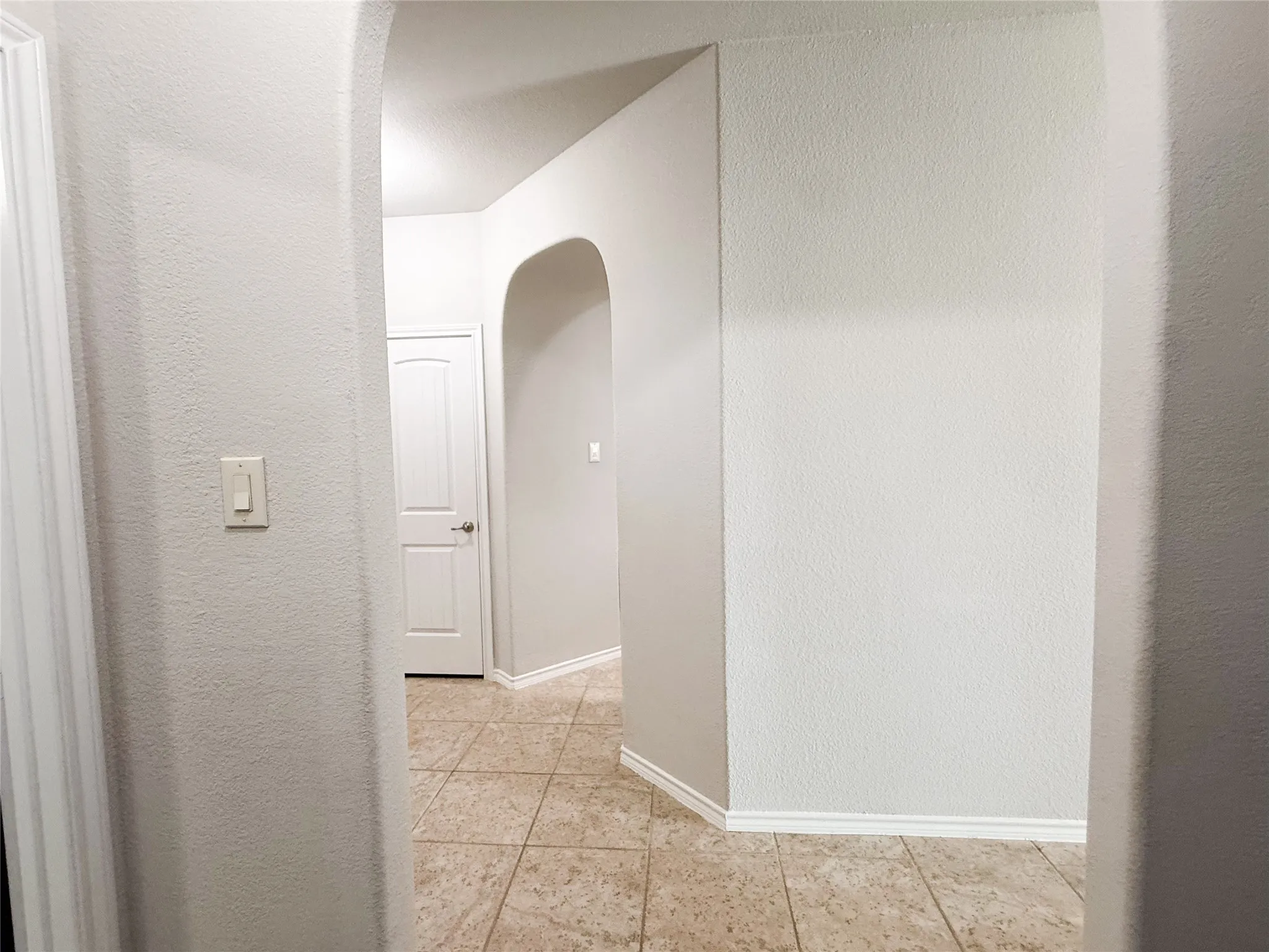Hallway featuring arched entryways, neutral wall tones, white trim, and square-tiled flooring