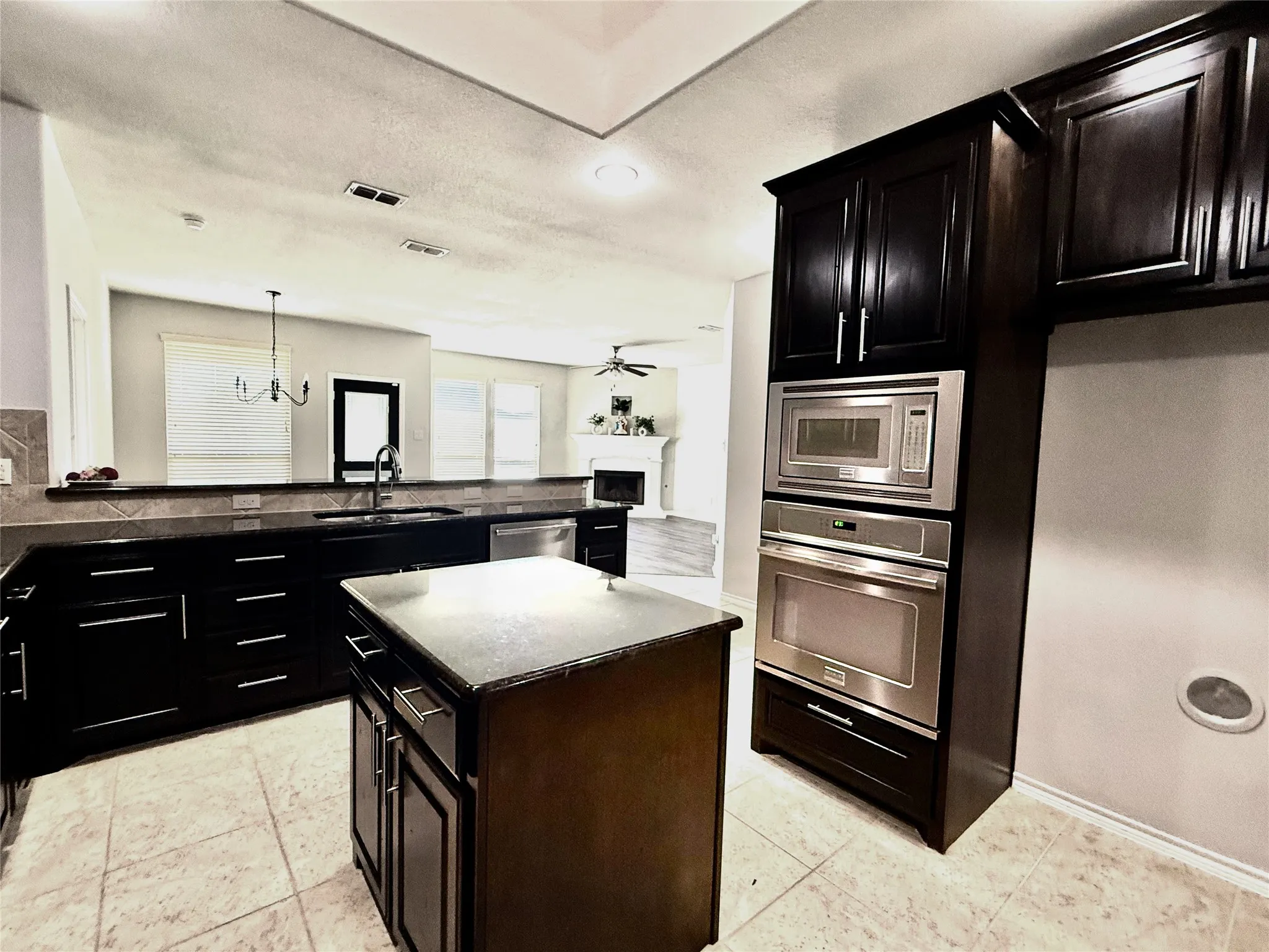 Contemporary kitchen featuring dark wood cabinetry, a central island with a solid surface countertop, and integrated stainless steel appliances including a microwave and oven