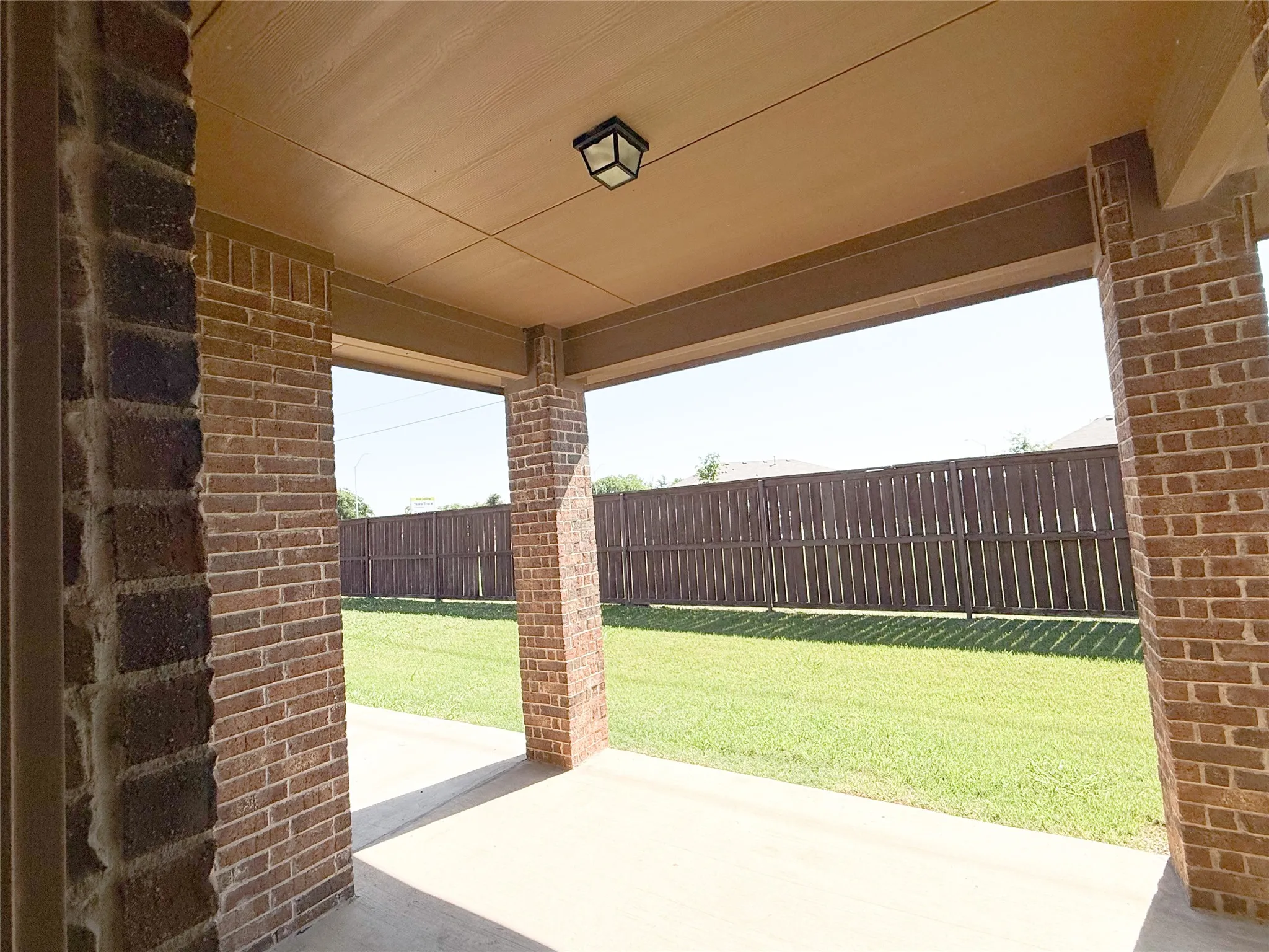 Covered patio featuring brick columns, concrete flooring, and an overhead light fixture