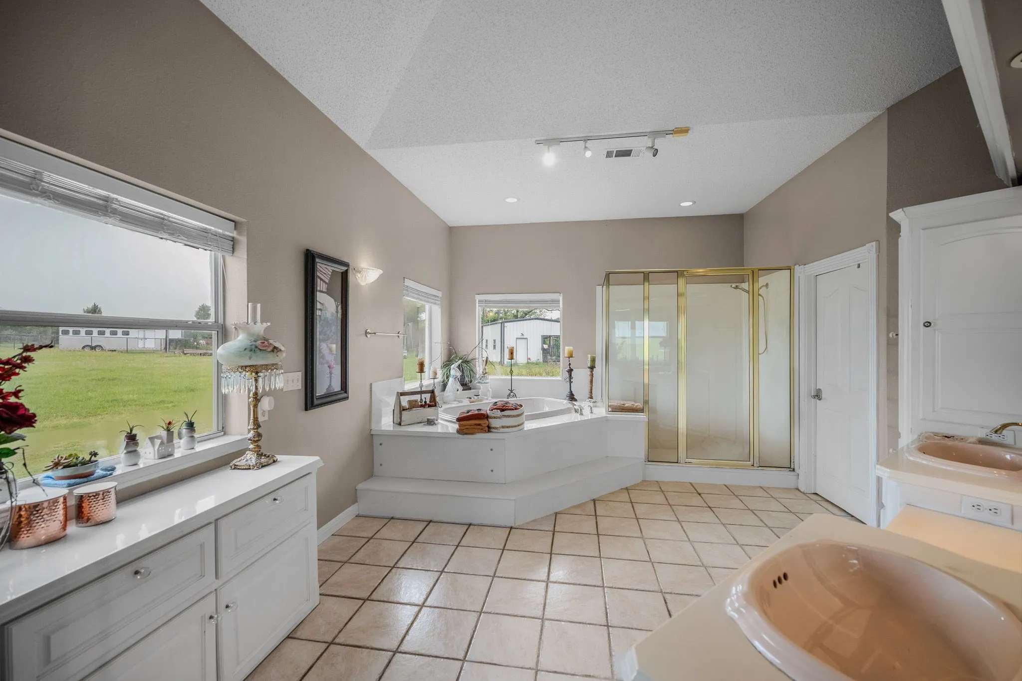 Spacious bathroom featuring a stepped corner tub, separate shower enclosure, dual vanity sinks, and tile flooring