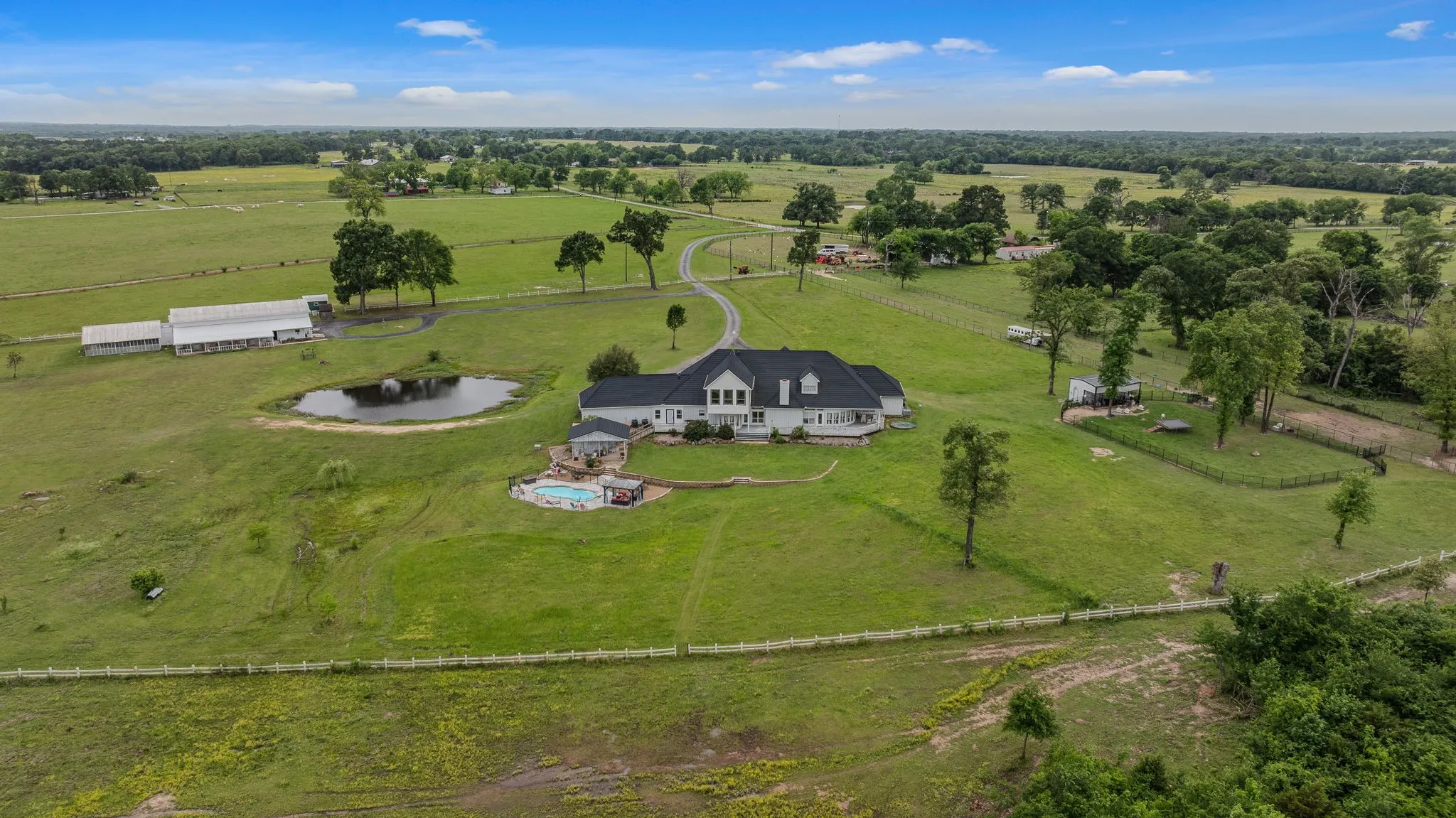 Expansive estate featuring a large main residence, an outdoor swimming pool, a private pond, and a multi-stall barn structure