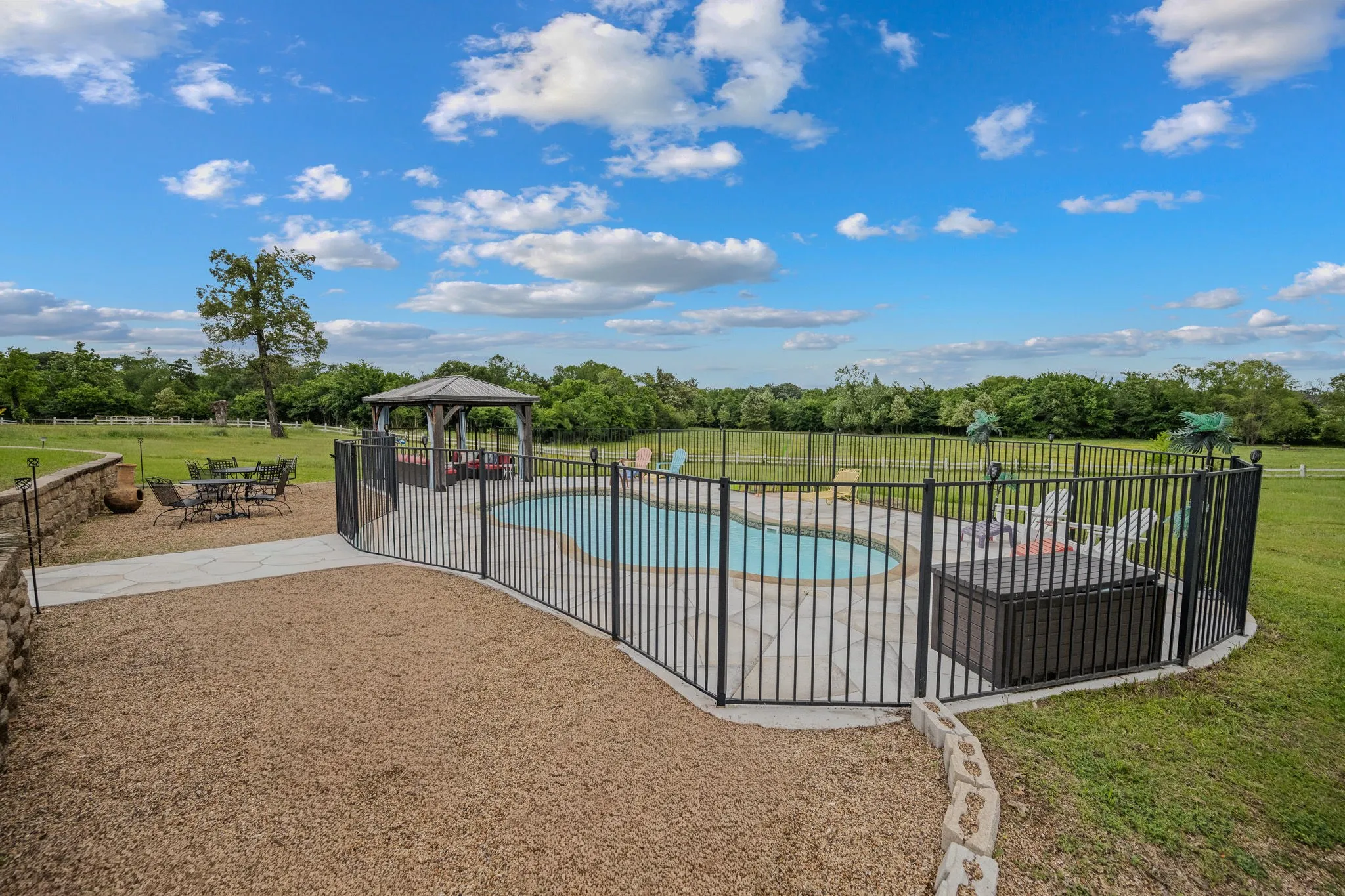 In-ground swimming pool with surrounding black metal fencing and an adjacent gazebo