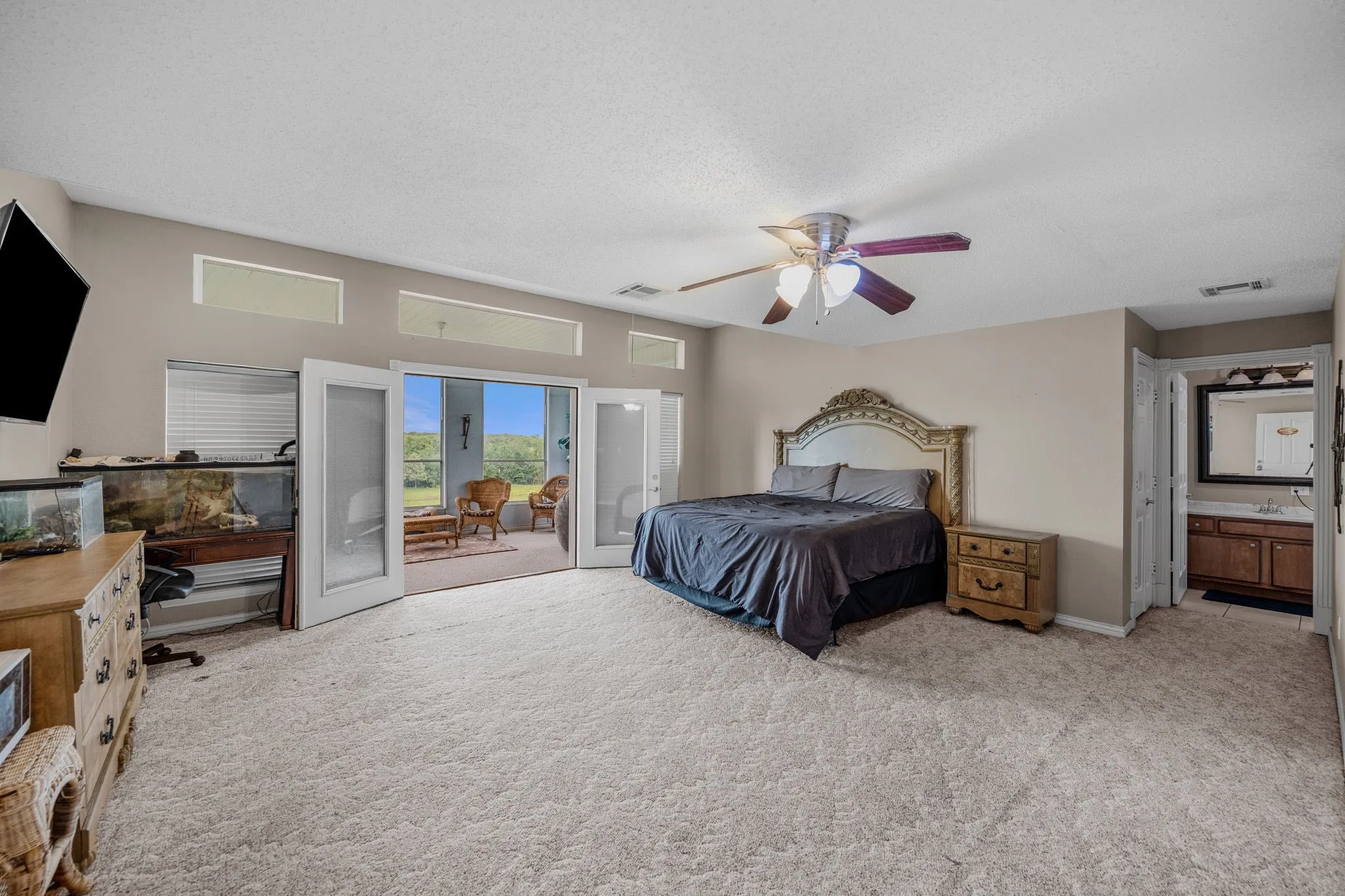 Spacious room featuring broadloom carpeting, a ceiling fan with integrated lighting, transom windows, and double French doors opening to an enclosed patio