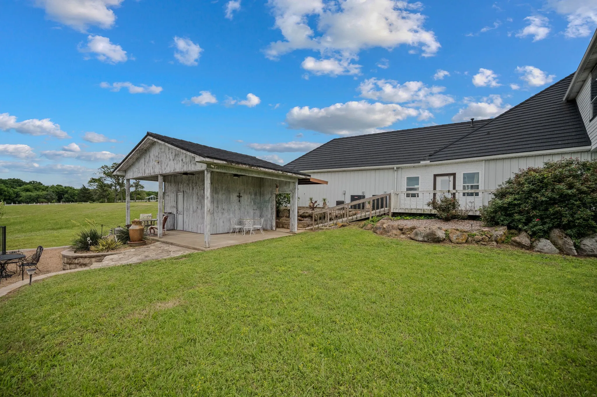 Expansive green lawn with a white wood-sided outbuilding featuring a covered porch