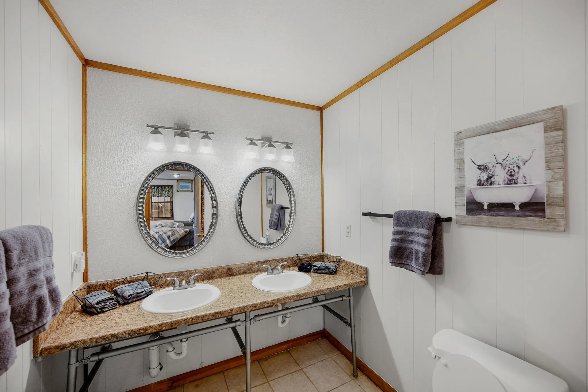 Bathroom featuring a double vanity with oval mirrors, two undermount sinks, and a speckled countertop