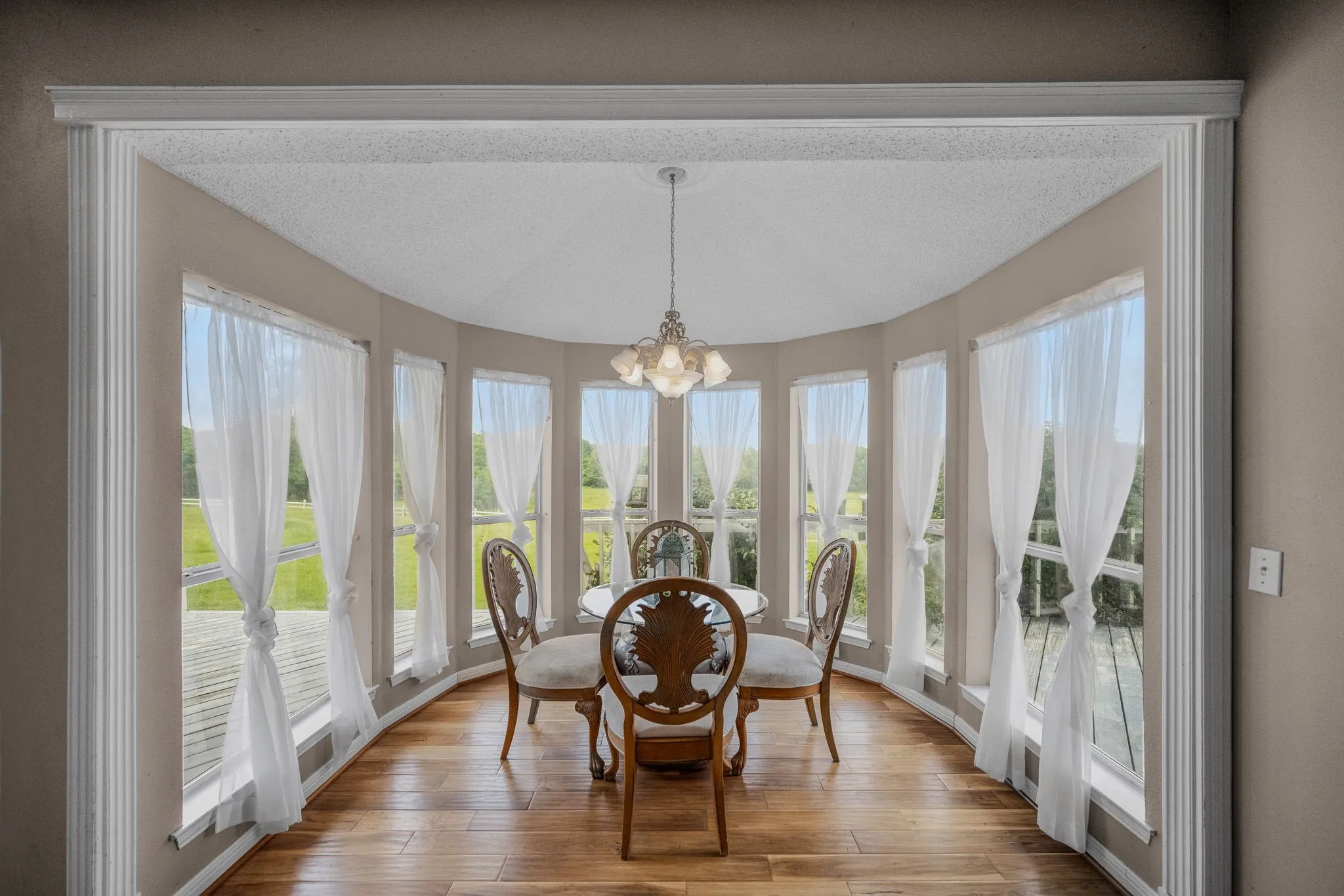 Bay window dining space featuring wood-finish flooring, a decorative chandelier, and floor-to-ceiling windows overlooking exterior landscaping