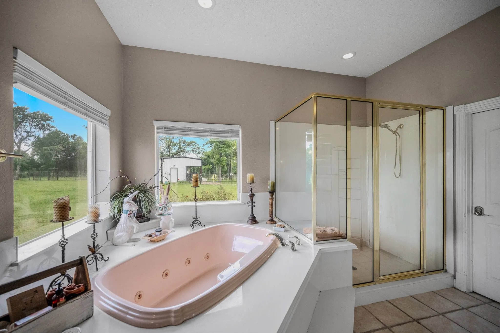 Soaking tub with jets, framed by multiple windows, alongside a glass-enclosed shower with gold-tone hardware