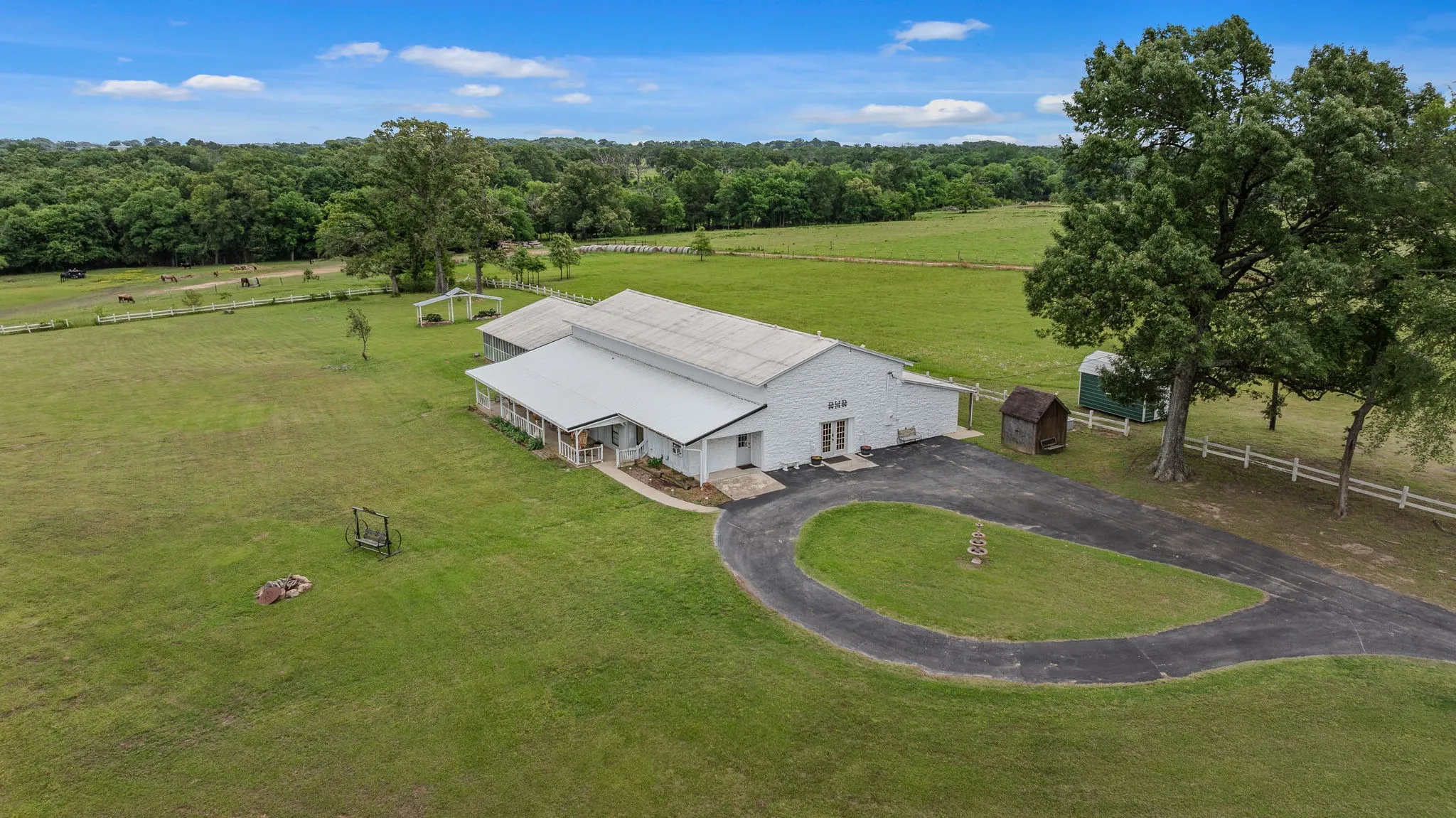 Expansive property featuring a white-sided structure with a metal roof, a wrap-around porch, and a circular driveway
