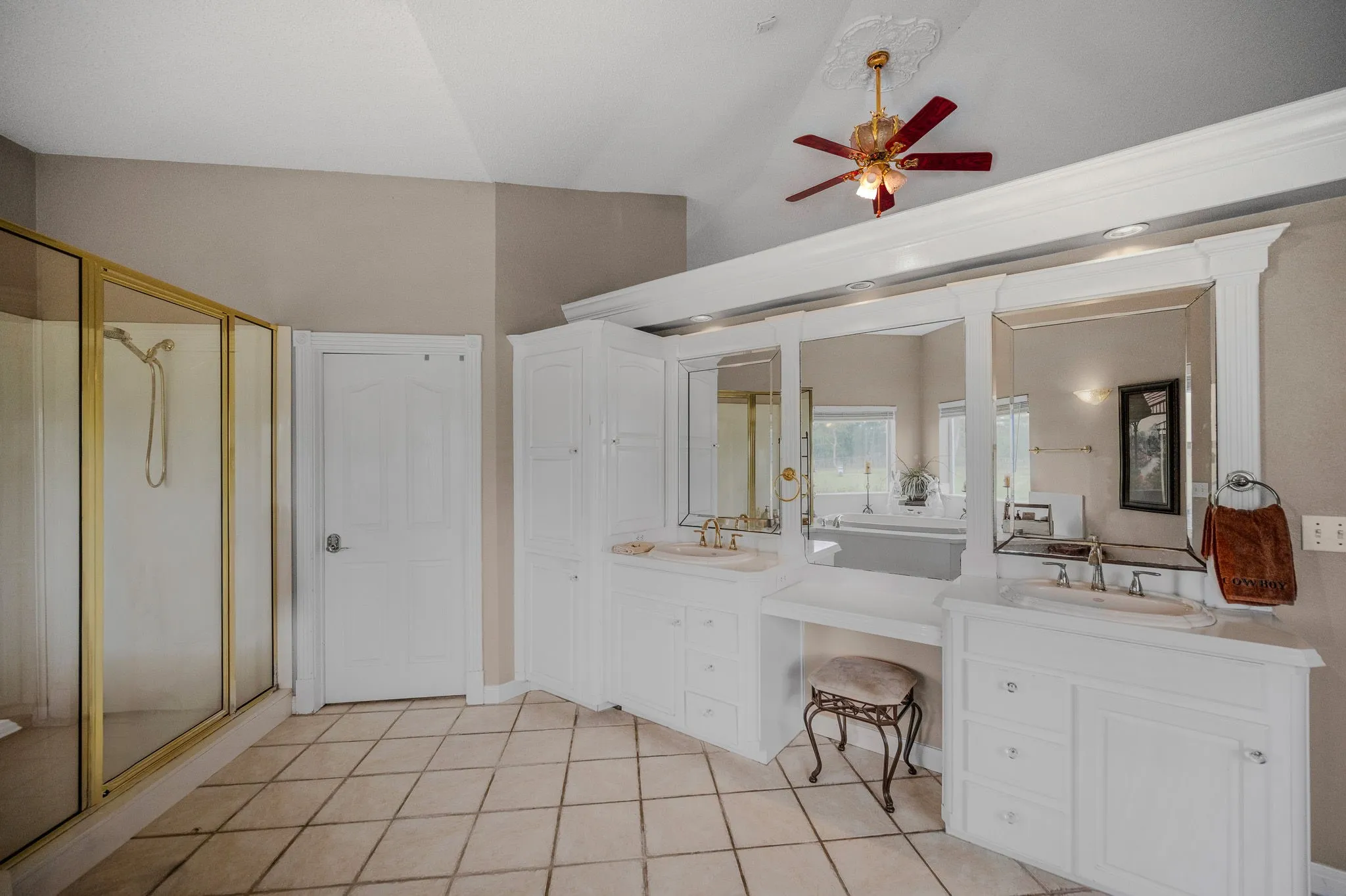 Bathroom featuring a dual vanity with integrated sinks and white cabinetry, a glass-enclosed shower, tile flooring, and a ceiling fan