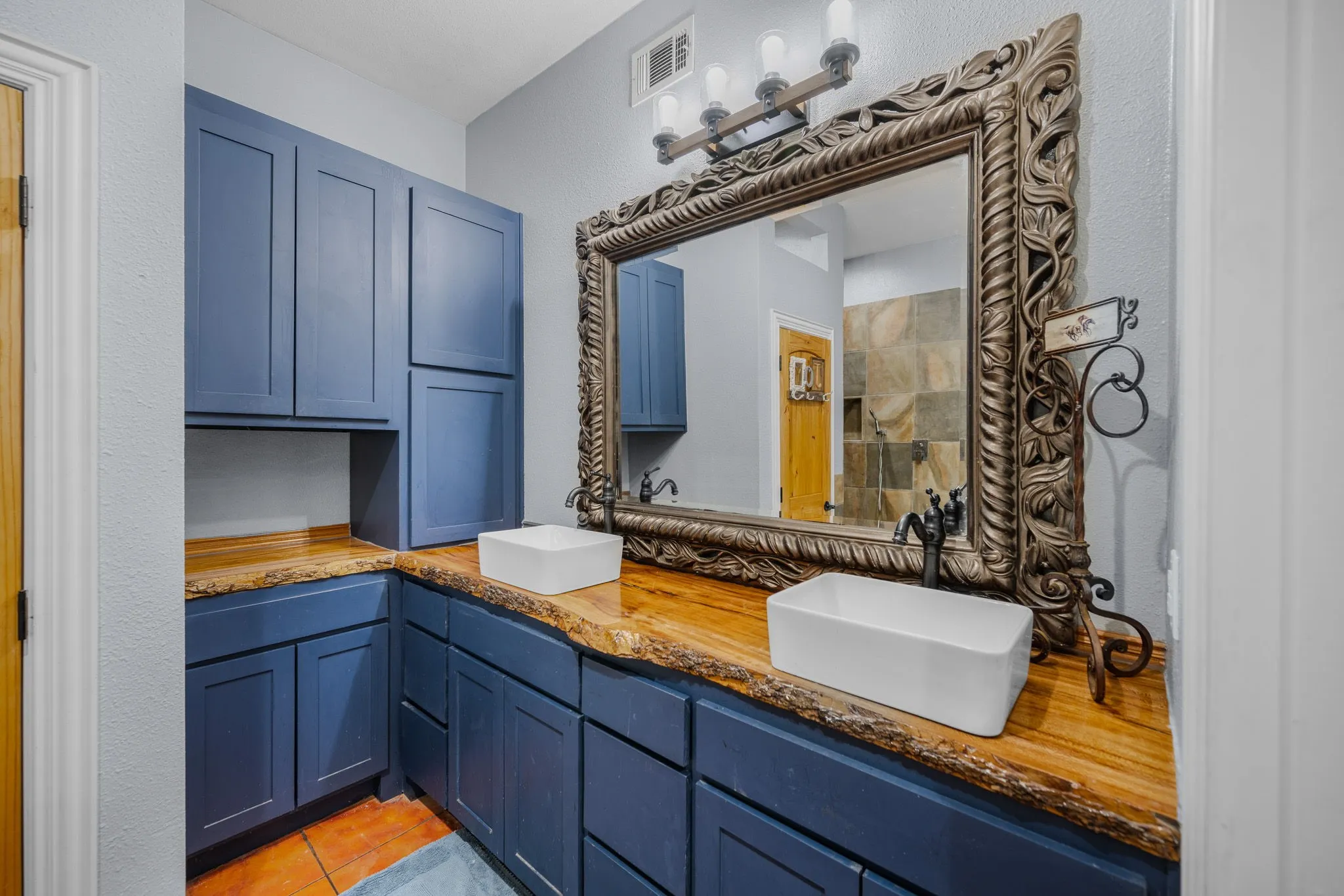 Bathroom featuring a dual vanity with rectangular vessel sinks, live-edge wood countertops, and blue cabinetry